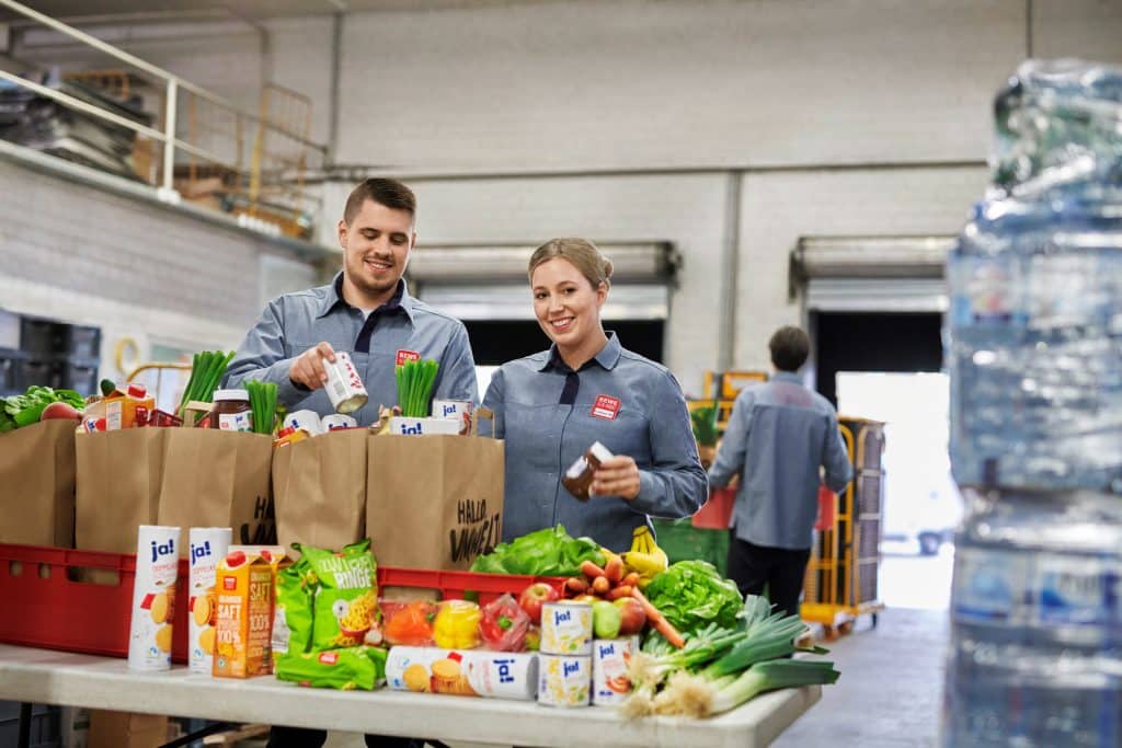 Zwei REWE-Mitarbeiter füllen Papiertüten mit Lebensmittel