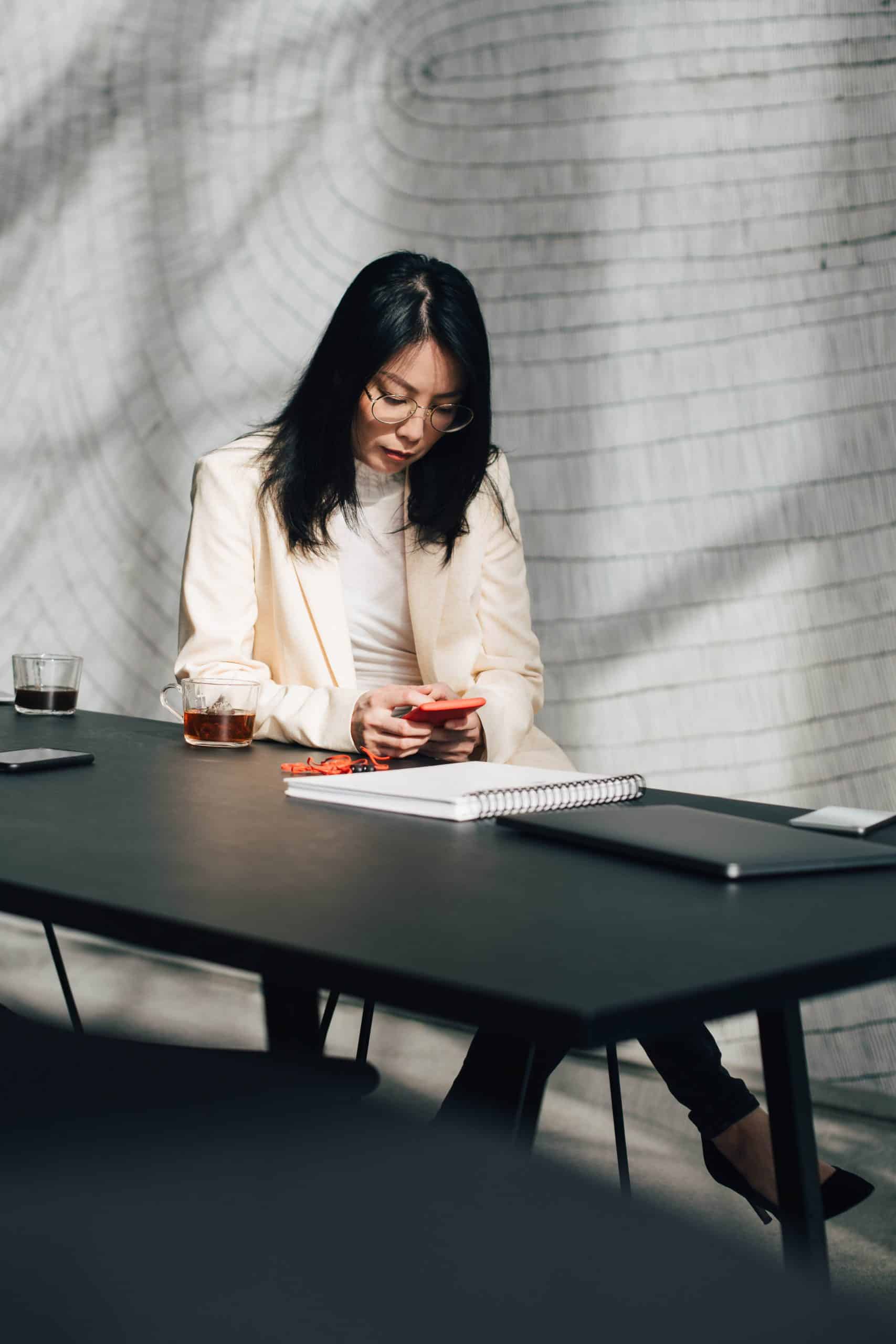 Eine Frau sitzt an einem Tisch und schaut auf ihr Smartphone. Ein Symbolbild für unser politisches Engagement bei der REWE Group
