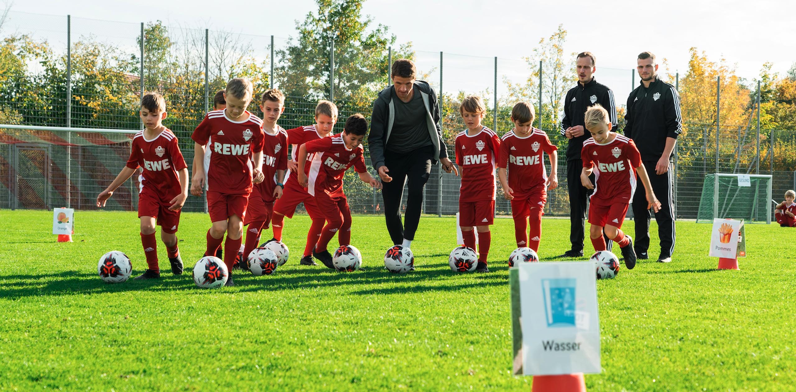 Eine Gruppe von Kindern, die gemeinsam mit Thomas Müller Fußball spielen