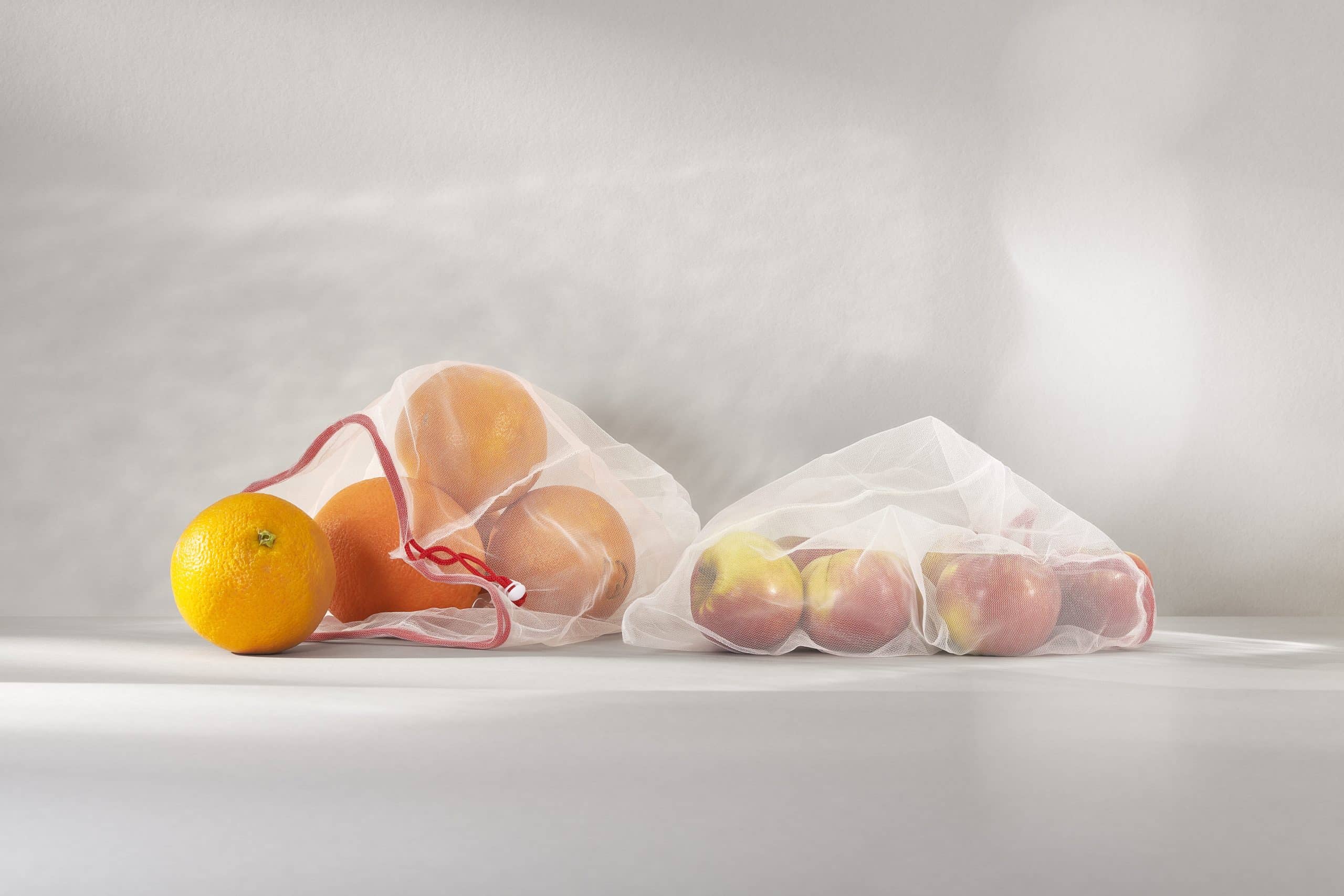 Orangen und Äpfel im Netz als Symbolbild für unsere Verpackungsstrategie: Vermeiden, verringern, verbessen