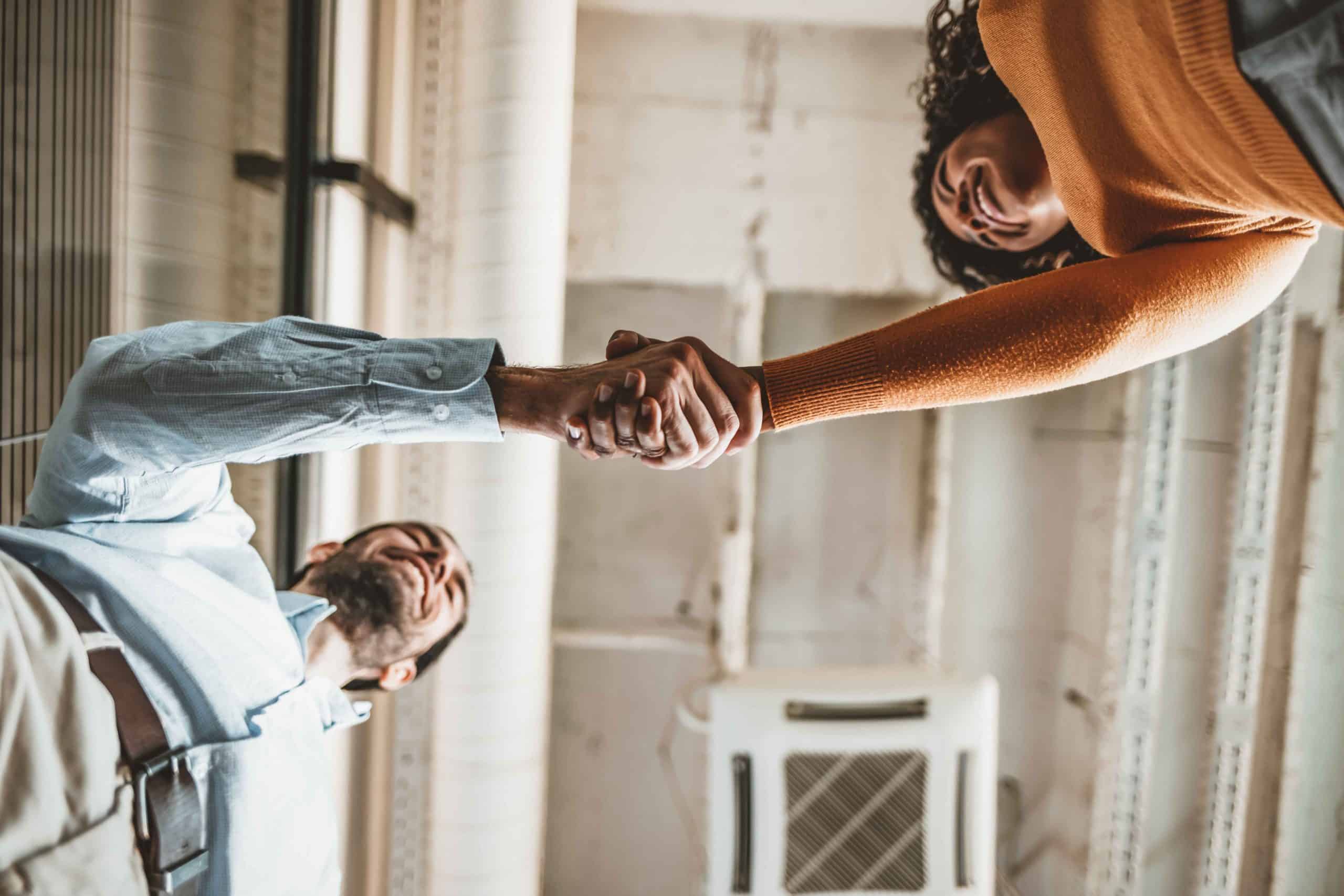 Two people seen from a low angle are shaking hands in a bright indoor setting.