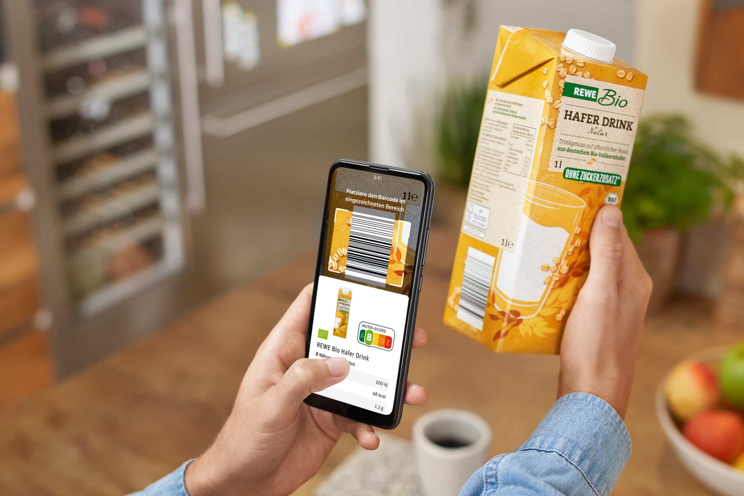 Eine Hafer-Drink-Verpackung wird hochgehalten, ein Smartphone scannt den Barcode. Auf dem Display des Handys ist der Nutri-Score zu sehen.