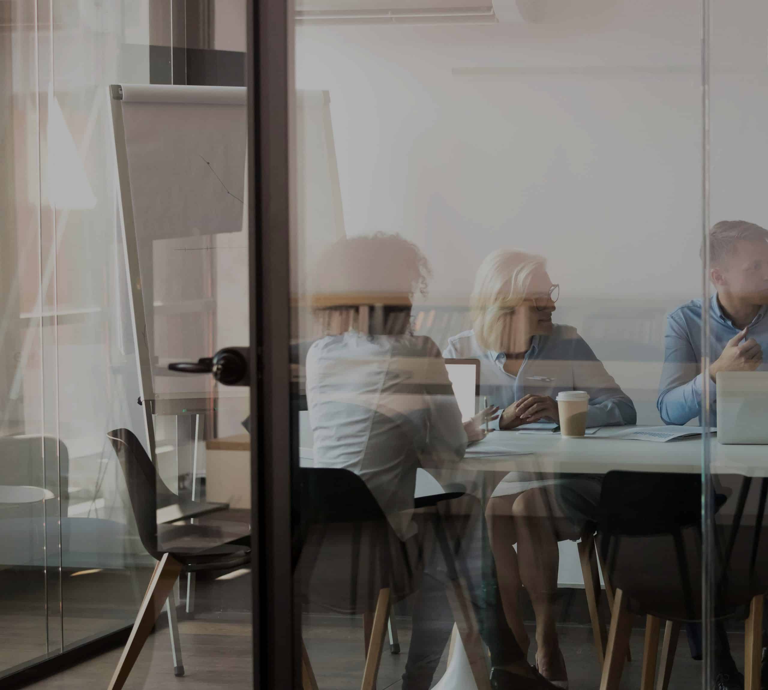 Two women and a man are sitting in a conference room with laptops and coffee