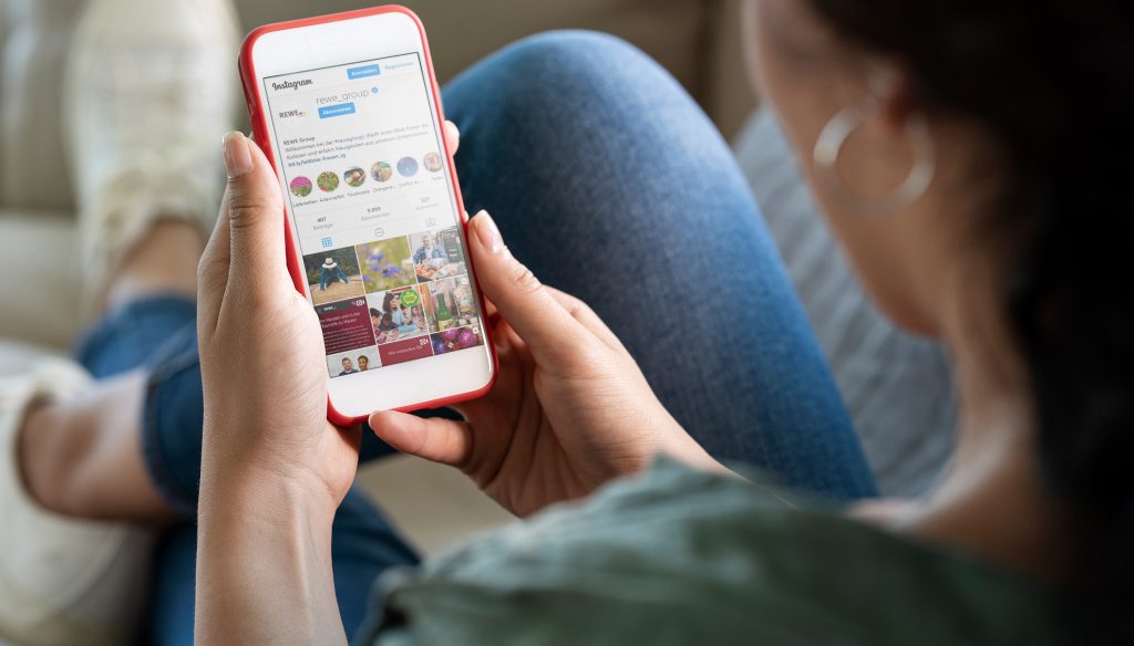 Eine junge Frau schaut sich auf ihrem Handy den REWE Group Instagram Feed an