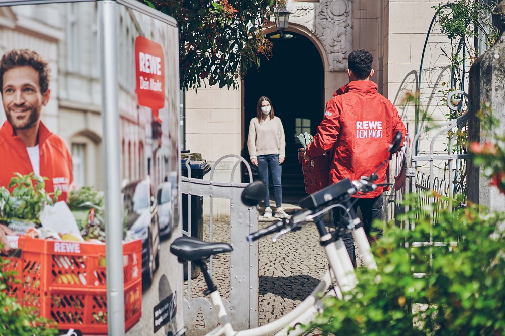 REWE-Lieferant übergibt bestellte Lebensmittel an Kundin