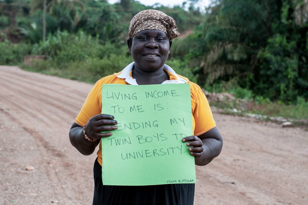Eine Farmerin hält ein Schild hoch, auf dem geschrieben steht: „Existenzsichernder Lohn bedeutet für mich, meine Zwillingssöhne zur Universität schicken zu können.“