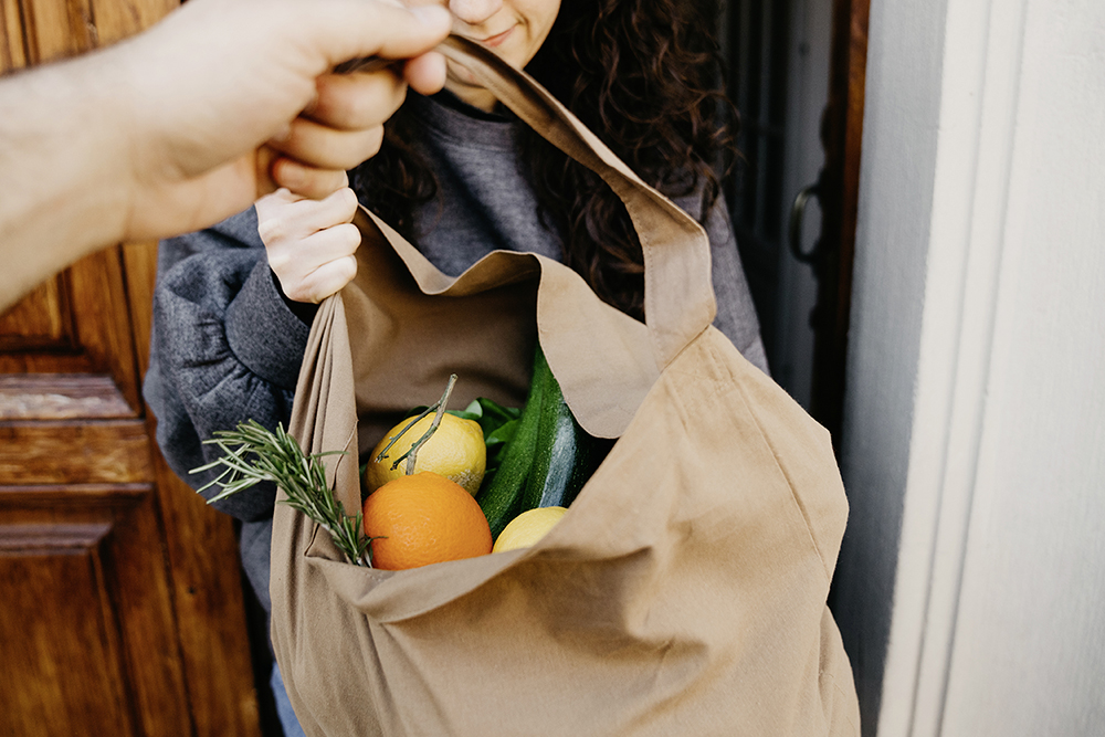 A bag of fruits and vegetables is handed to a woman.