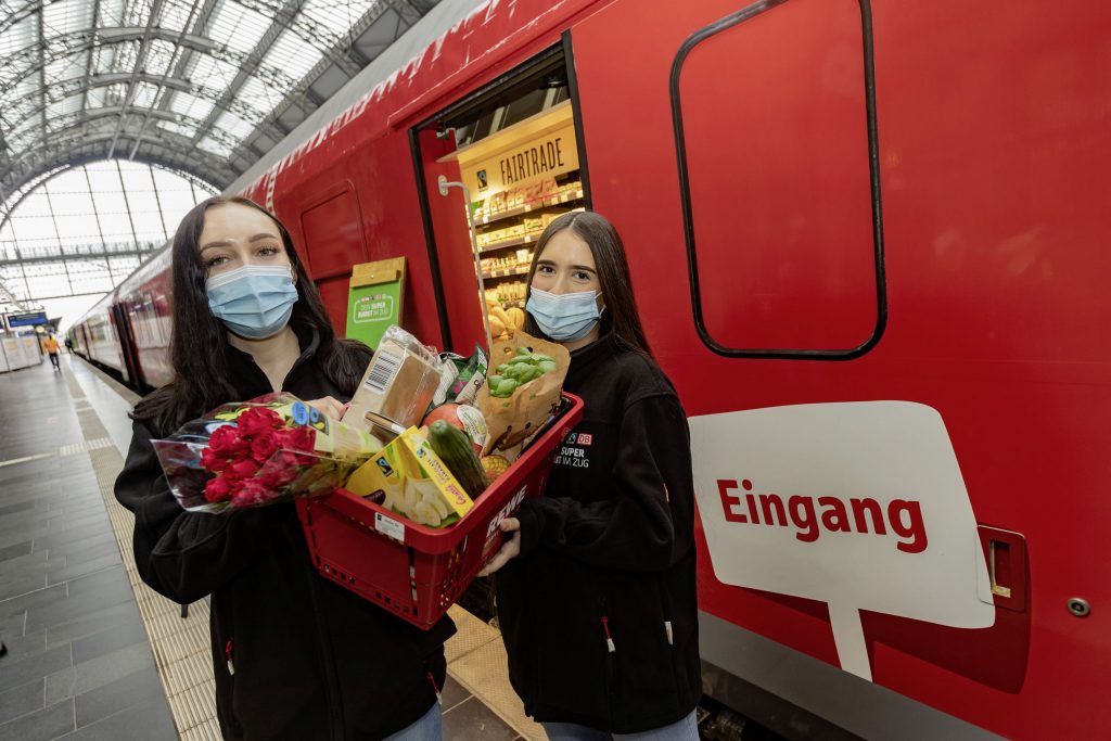 Zwei REWE Auszubildende stehen mit Ware vor dem Supermarktzug
