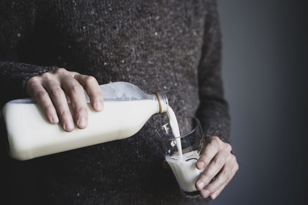 Person mit Milchflasche in der Hand schüttet sich ein Glas ein