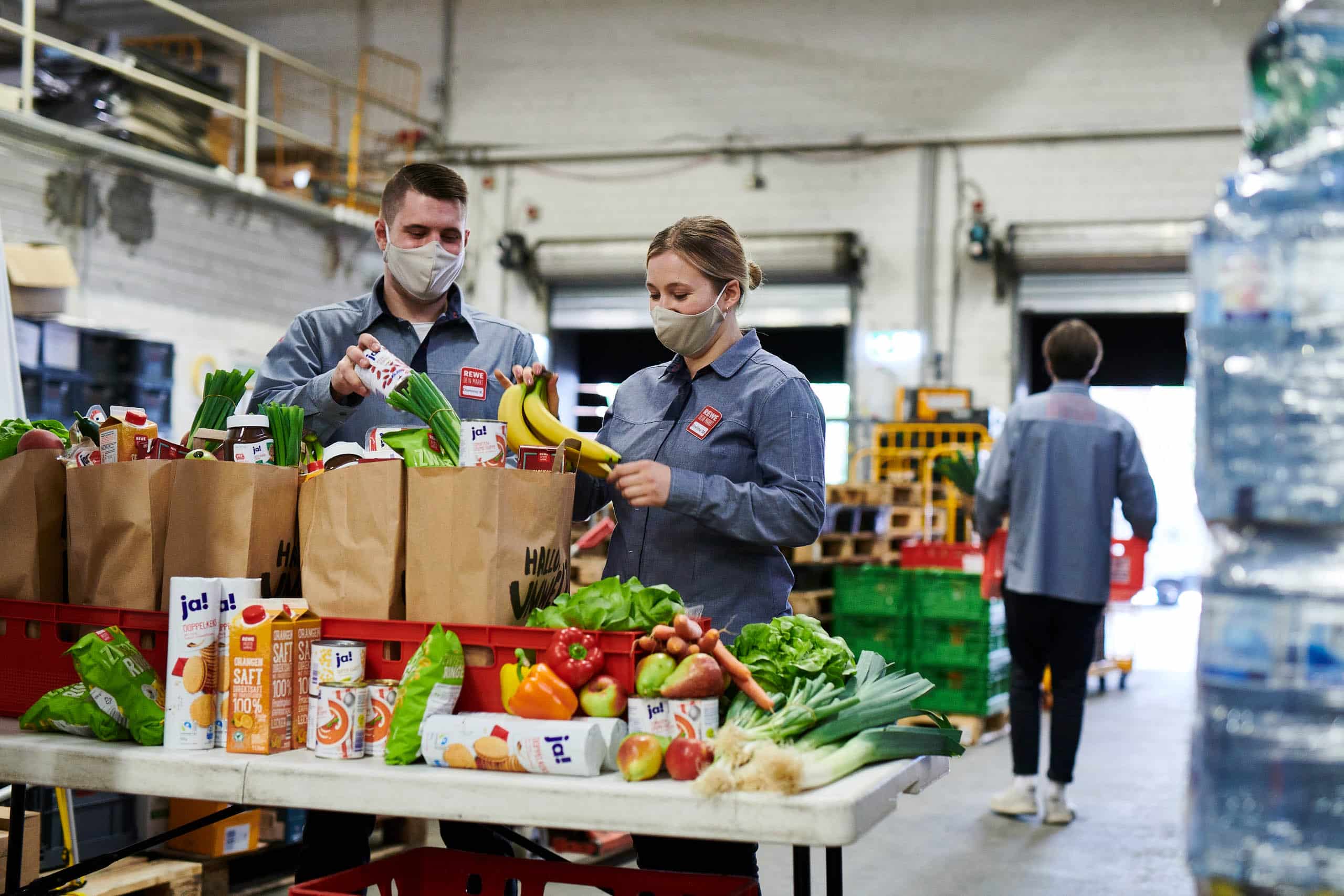 Zwei REWE Mitarbeitende packen Lebensmittel in REWE Papier-Tüten