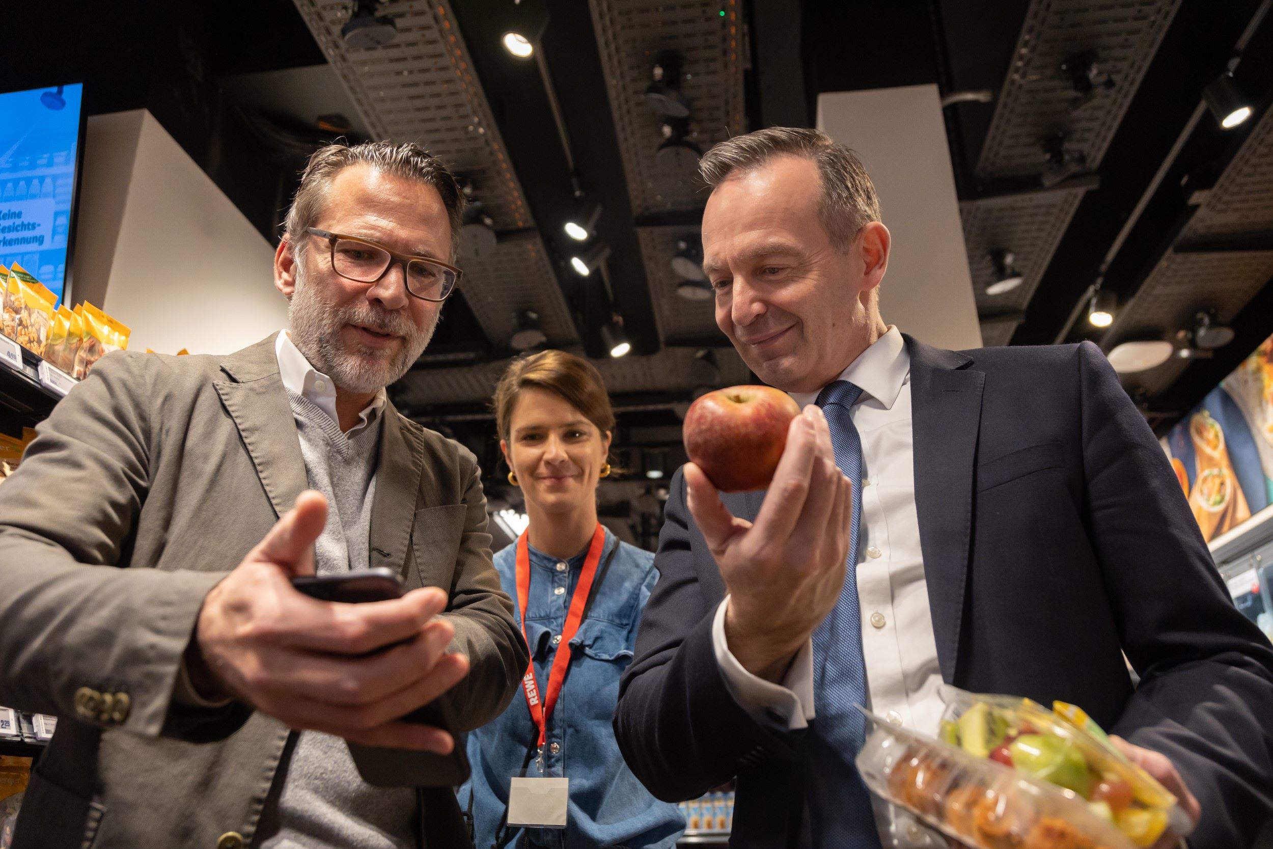 Volker Wissing und Christoph Eltze im Markt mit Smartphone und Apfel in den Händen.
