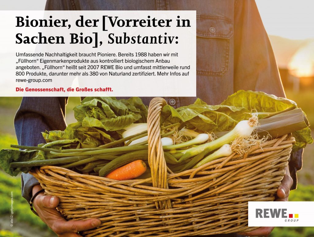 Ein Mitarbeiter hält einen Korb mit Gemüse. Der Titel: Bionier, der (Vorreiter in Sachen Bio), Substantiv