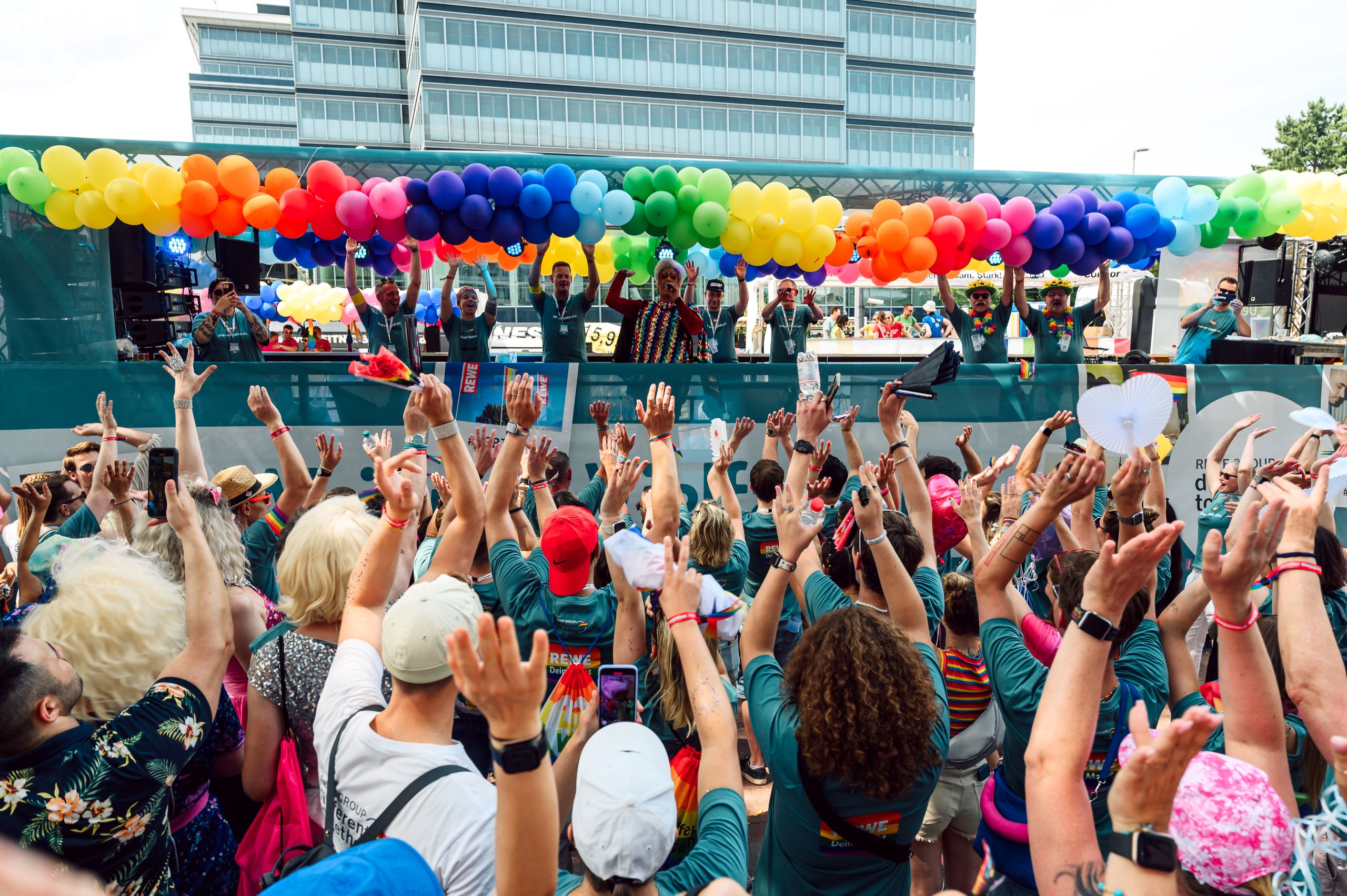 Menschenmenge auf dem Christopher Street Day in Köln vor einem Wagen mit Regenbogenfarbenen Ballons.