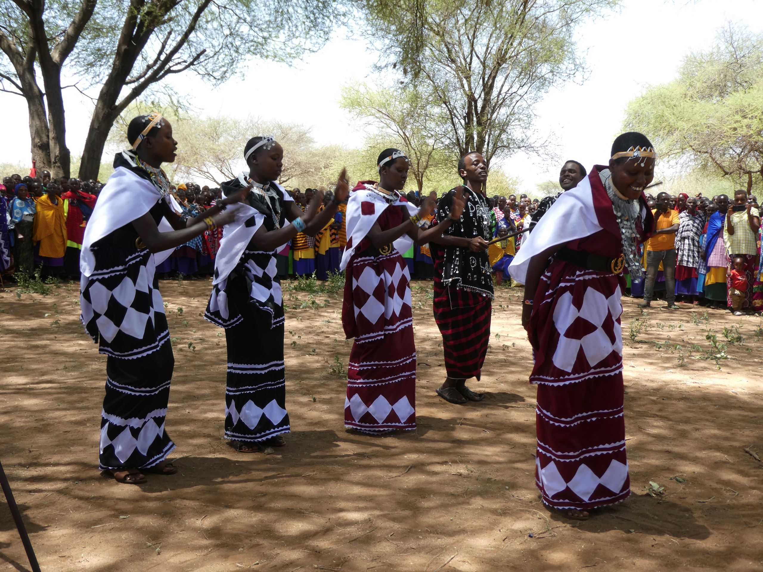 Personen in traditionellen afrikanischen Gewändern auf einem Platz umgeben von einer Zuschauermenge