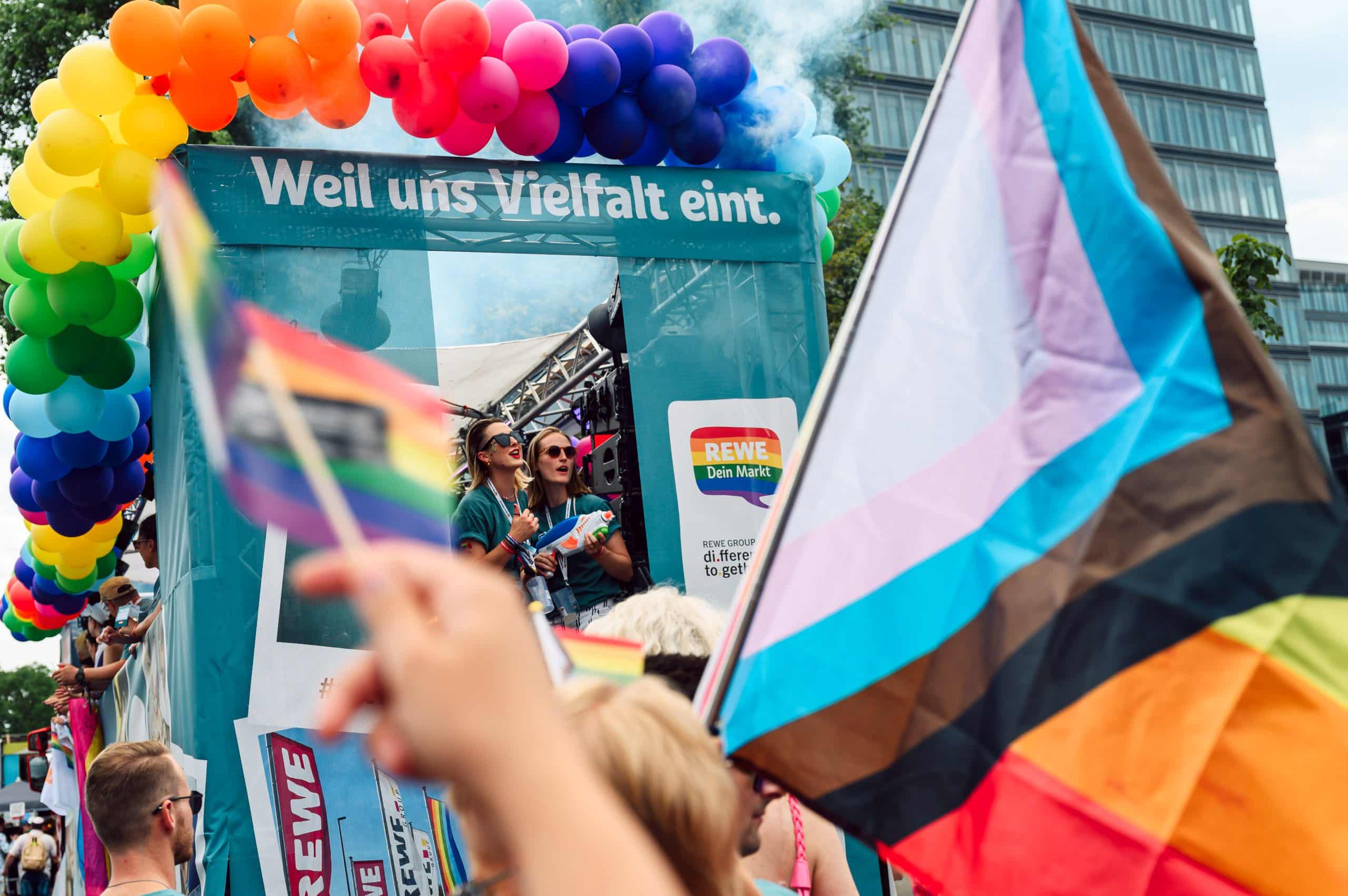 Wagen auf dem CSD mit dem Aufdruck "Weil uns Vielfalt eint." mit einer LGBTQI+ Flagge im Vordergrund und einer Menschenmenge.