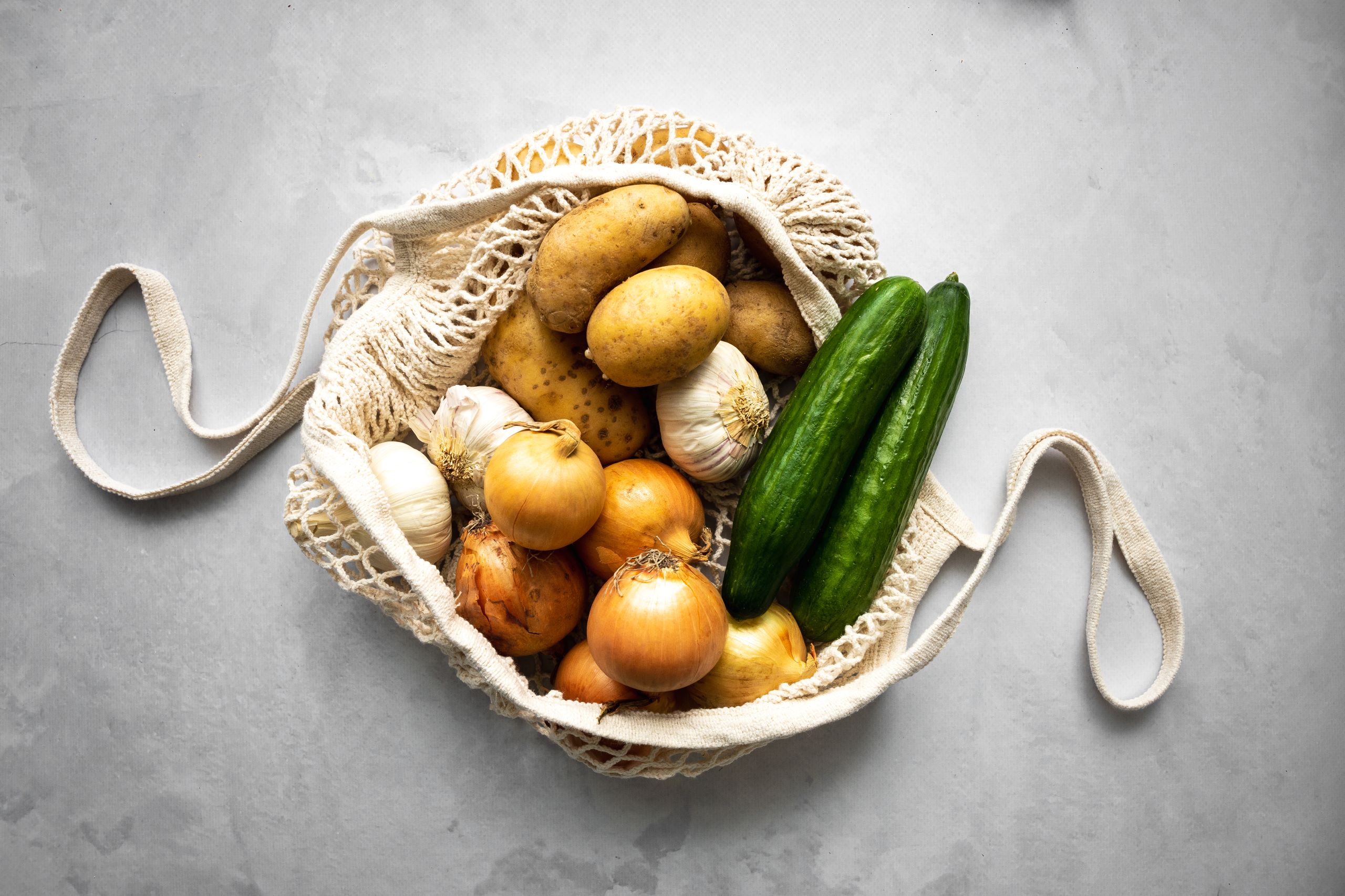 Einkaufsnetz von oben mit Kartoffeln, Gurken, Zwiebel und Knoblauch