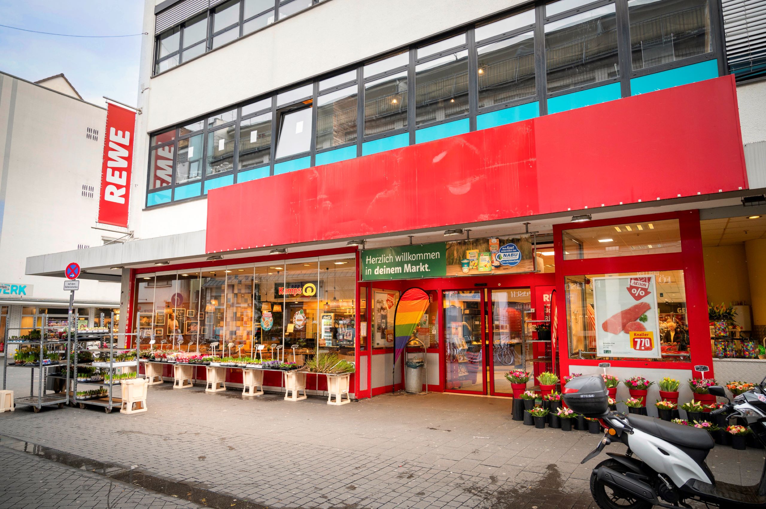 Außenansicht des REWE-Markt Ridders mit Regenbogenflagge am Eingang.