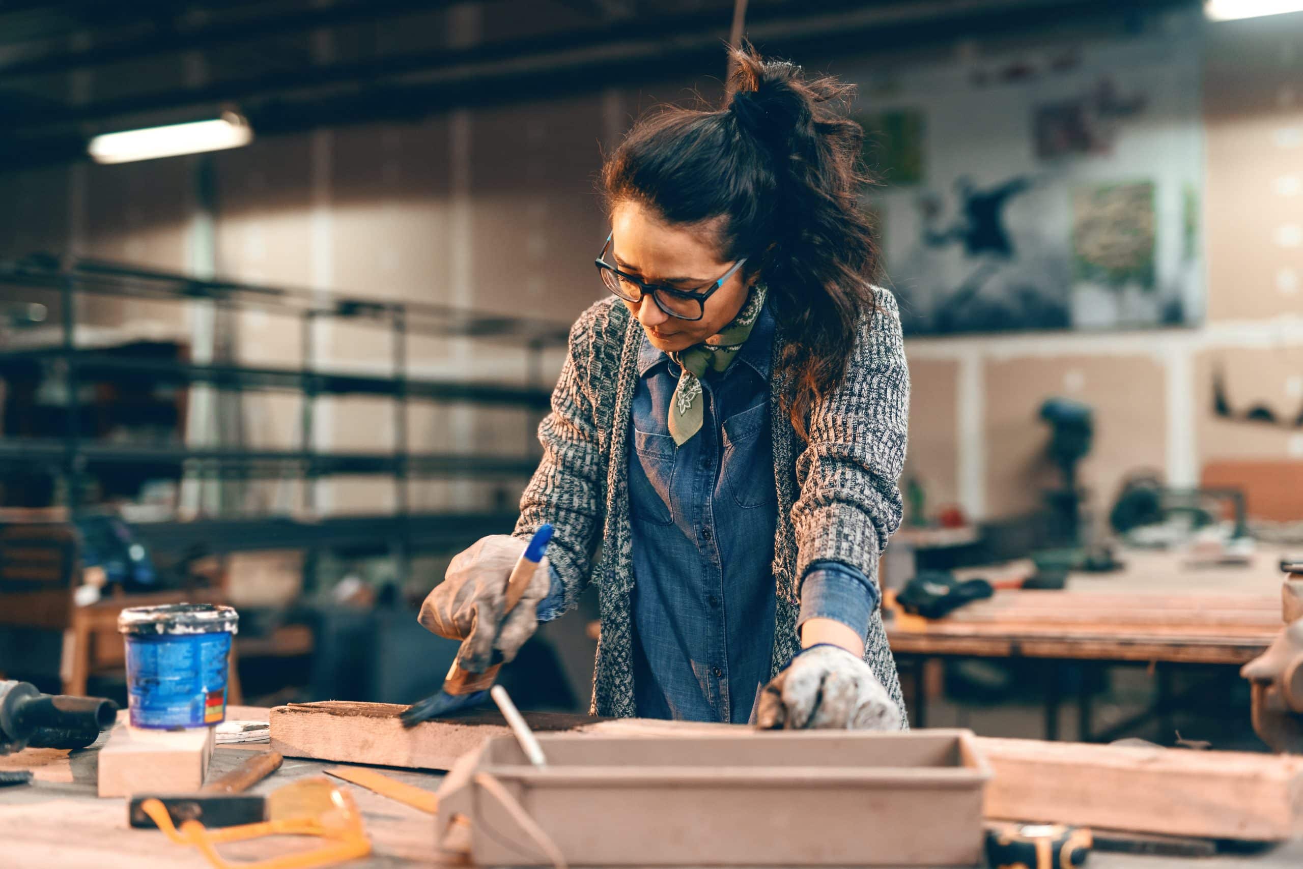 Eine Frau streicht ein Stück Holz in der Werkstatt.