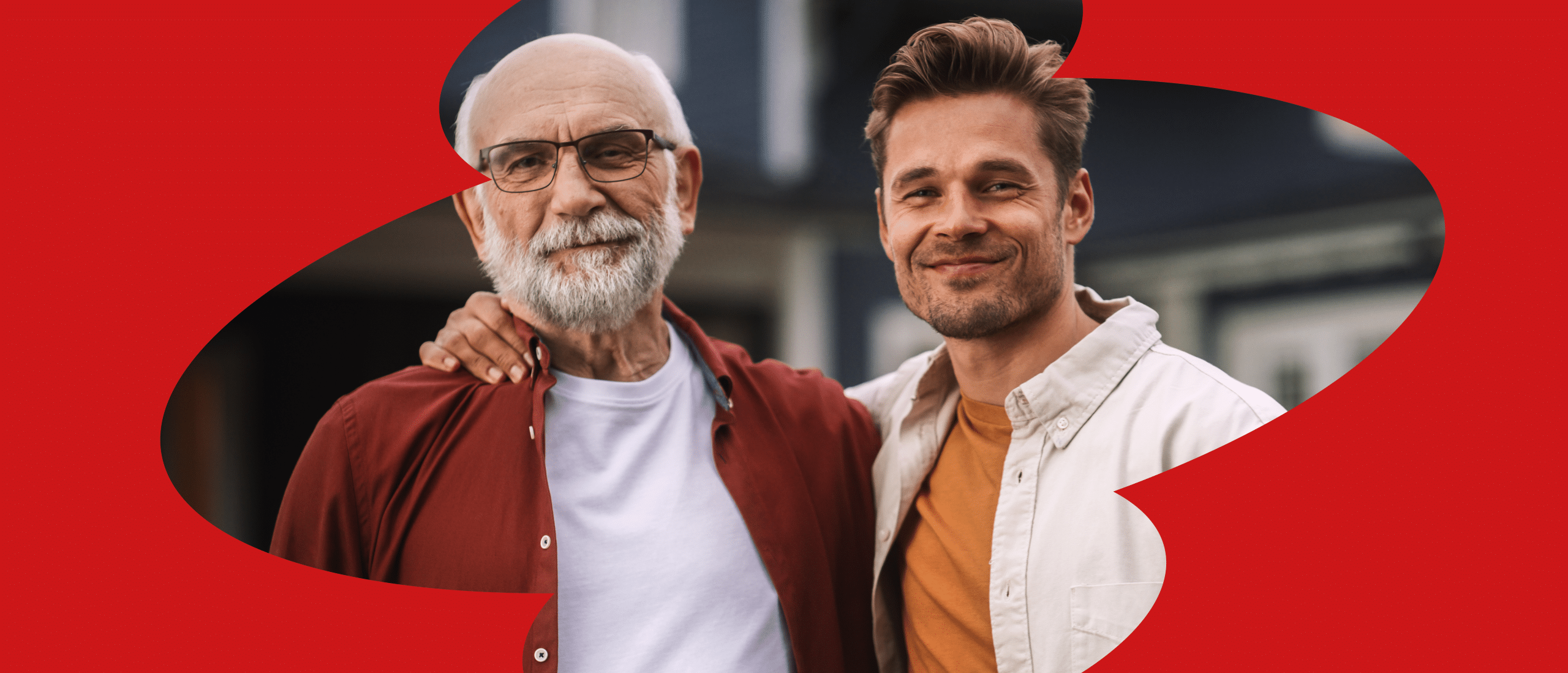 Älterer und jüngerer Mann stehen Arm in Arm und lächeln in die Kamera.