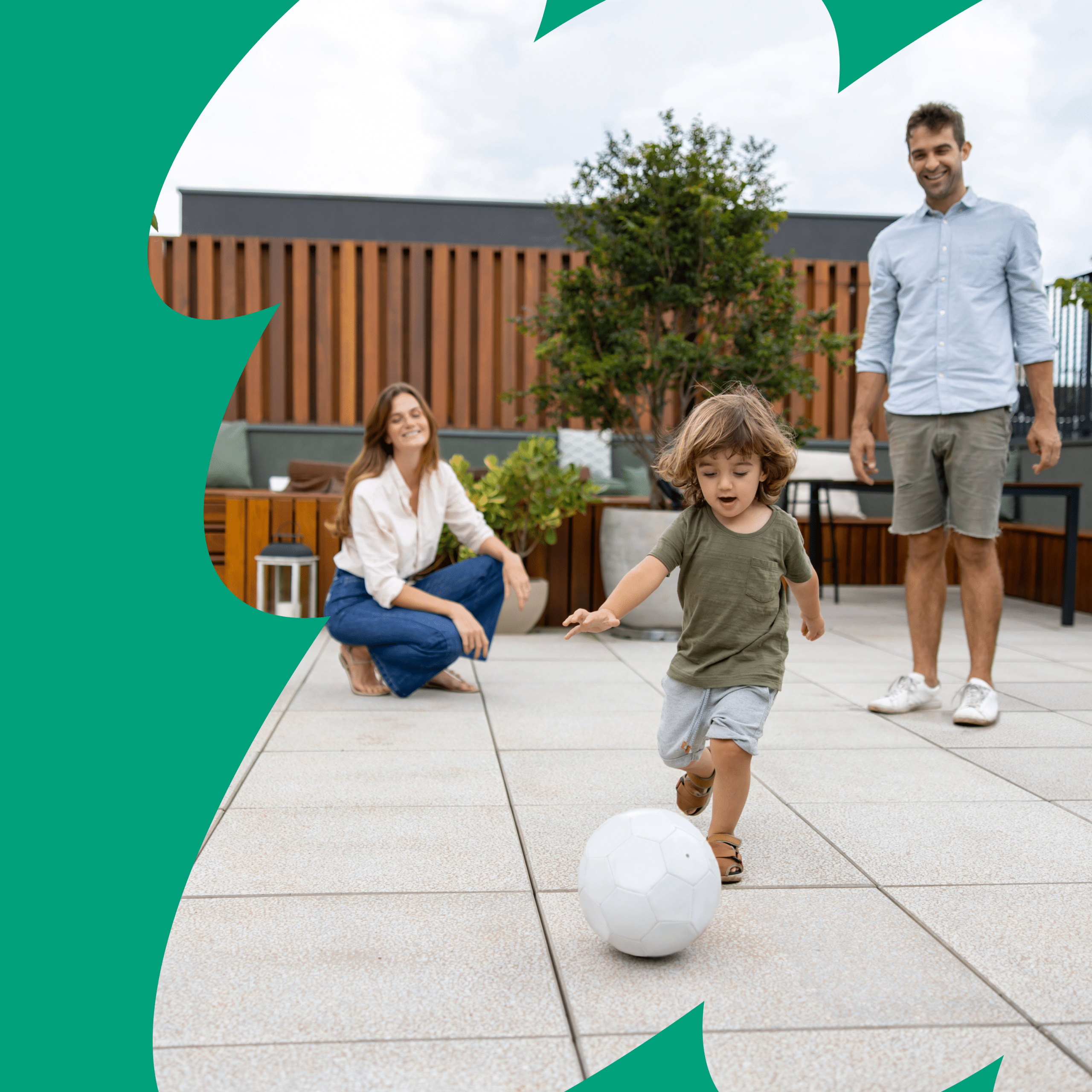 Glückliche Eltern spielen mit ihrem Kleinkind Fußball auf der Terrasse.