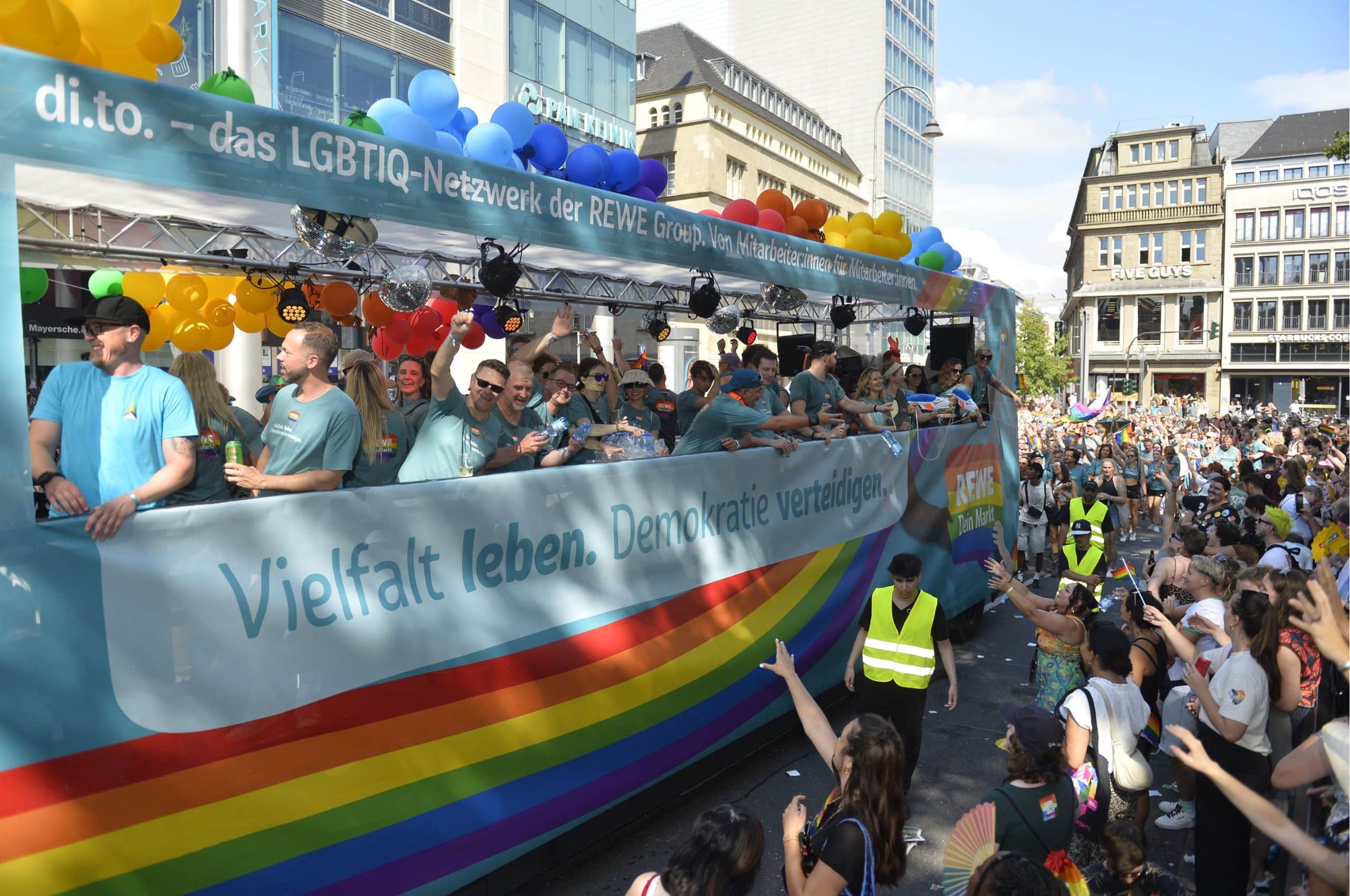 Waagen der REWE Group auf der ColognePride Parade mit Mitarbeitenden der REWE Group und dem Slogan 