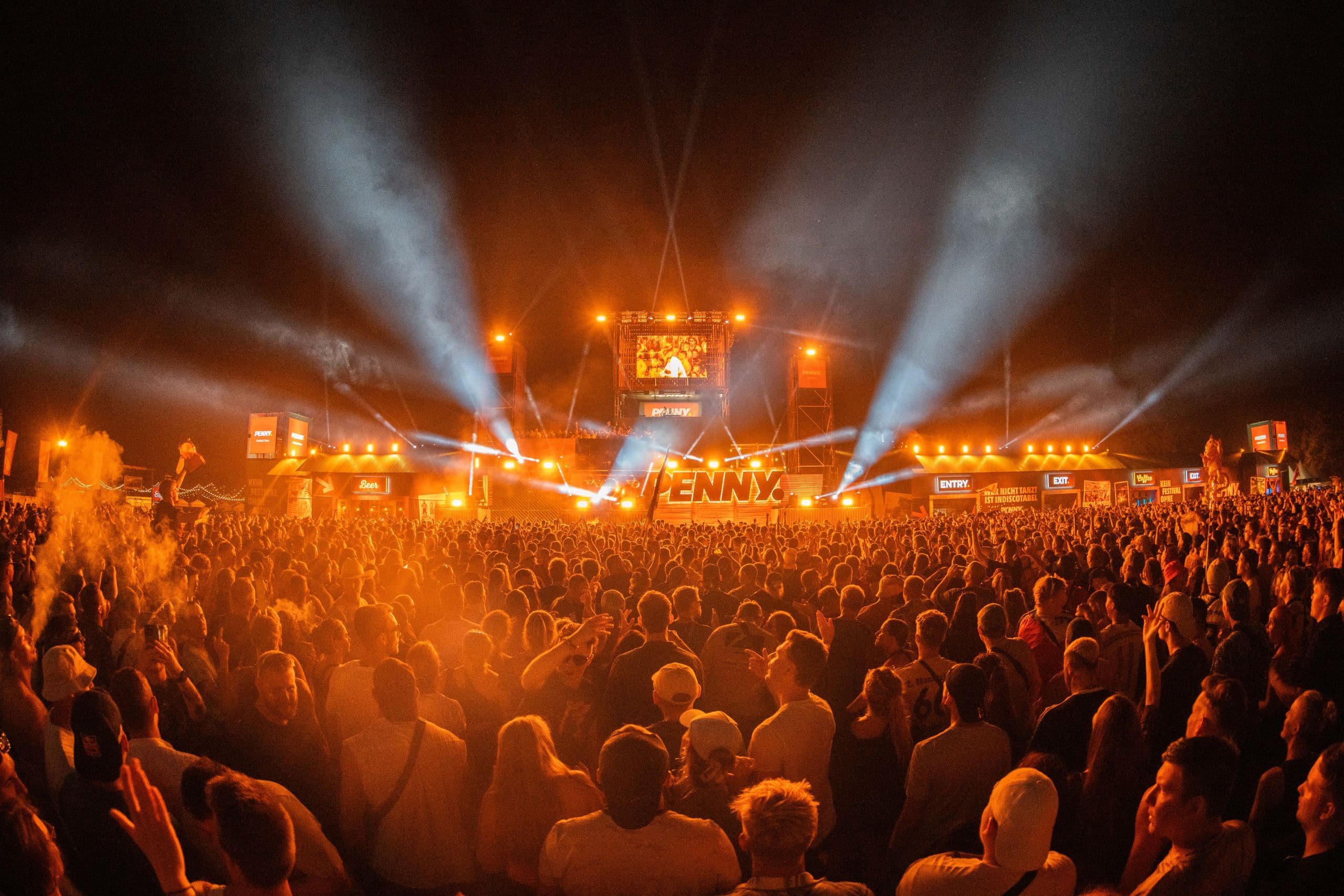 Menschenmenge auf dem Parookaville Festival vor dem DJ-Tower von PENNY. Orangenes Scheinwerferlicht.