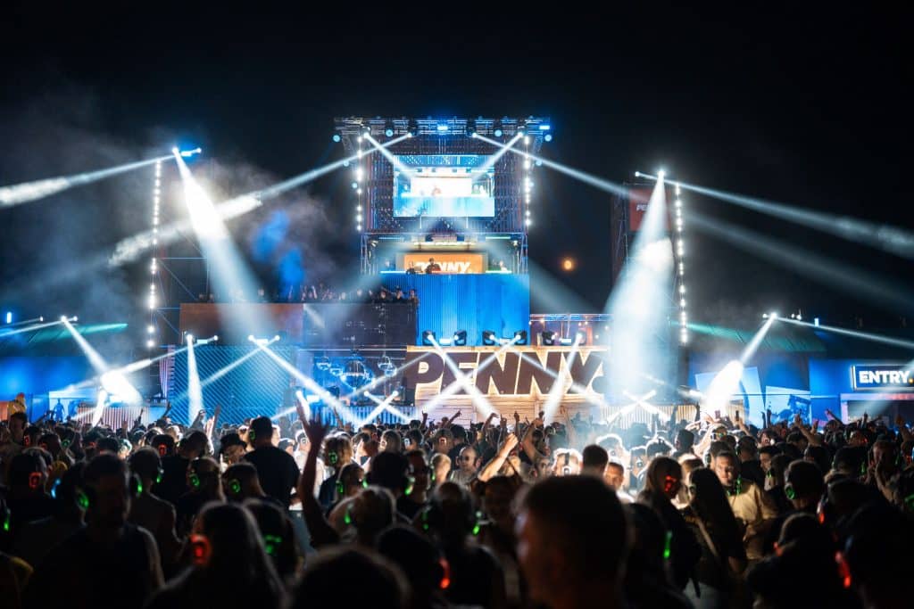 Menschenmenge auf dem Parookaville Festival vor dem DJ-Tower von PENNY. Weißes und blaues Scheinwerferlicht.