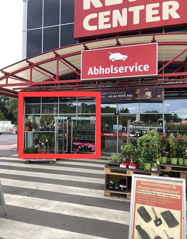 Außenansicht eines REWE Center mit Verkaufsfläche vor dem Eingang