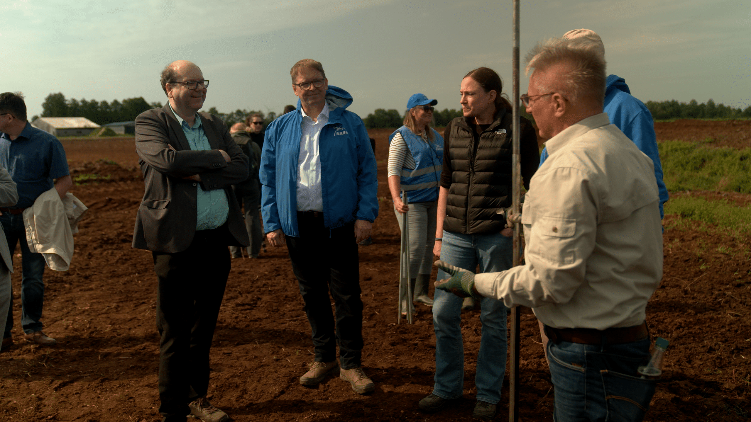 Fünf Personen, unter anderem Daniela Büchel, Mitglied des REWE Group Vorstandes, stehen im Kreis auf einem matschigen Feld und sind im Gespräch. Im Hintergrund sind weitere Personen zu sehen.