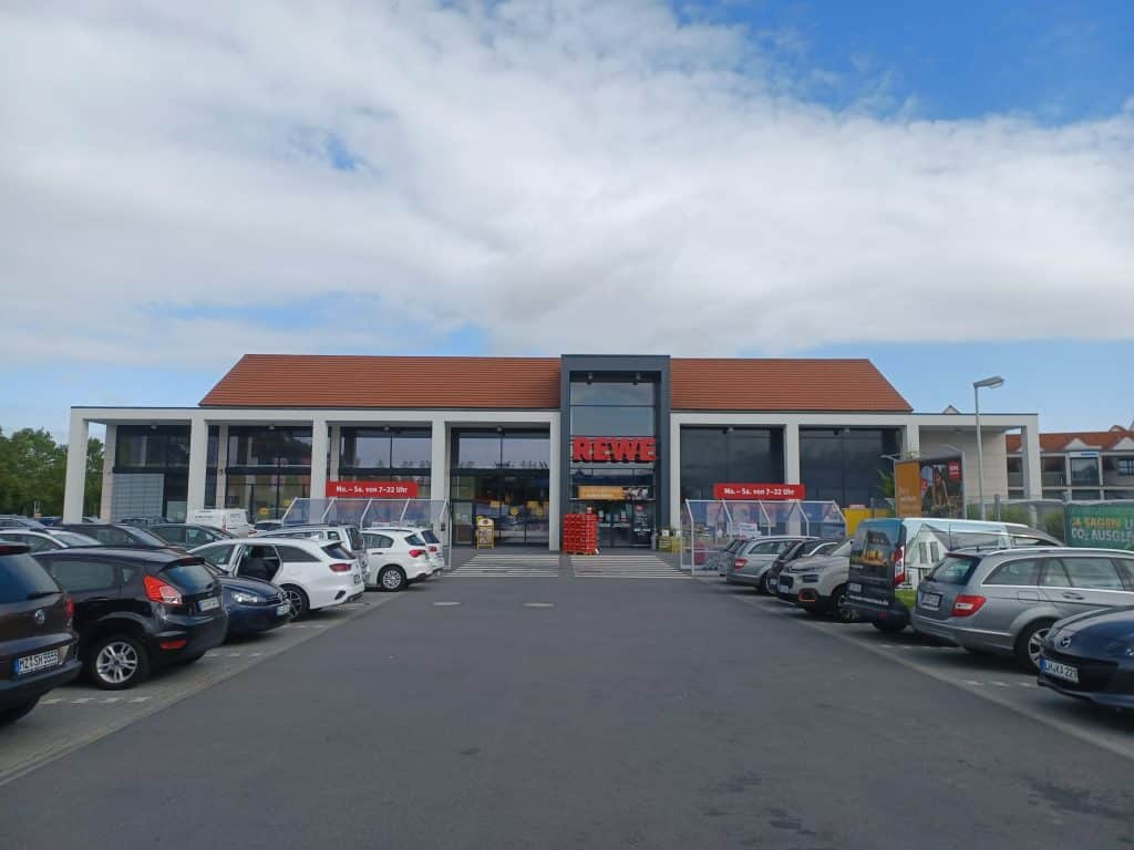 Außenansicht eines REWE Marktes mit Parkfläche.