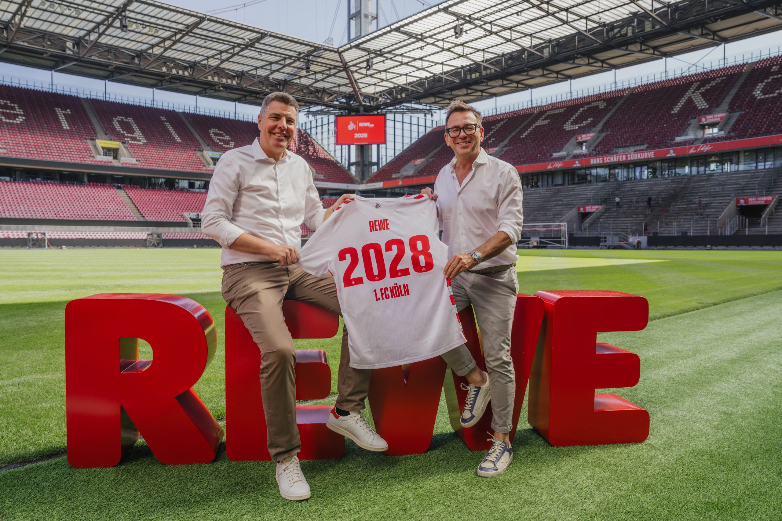Links: Dr. Sven Spork - Bereichsvorstand REWE Group und Rechts: Markus Rejek - Geschäftsführer Marketing & Vertrieb 1. FC Köln im Stadion mit dem Trikot des 1. FC Kölns.