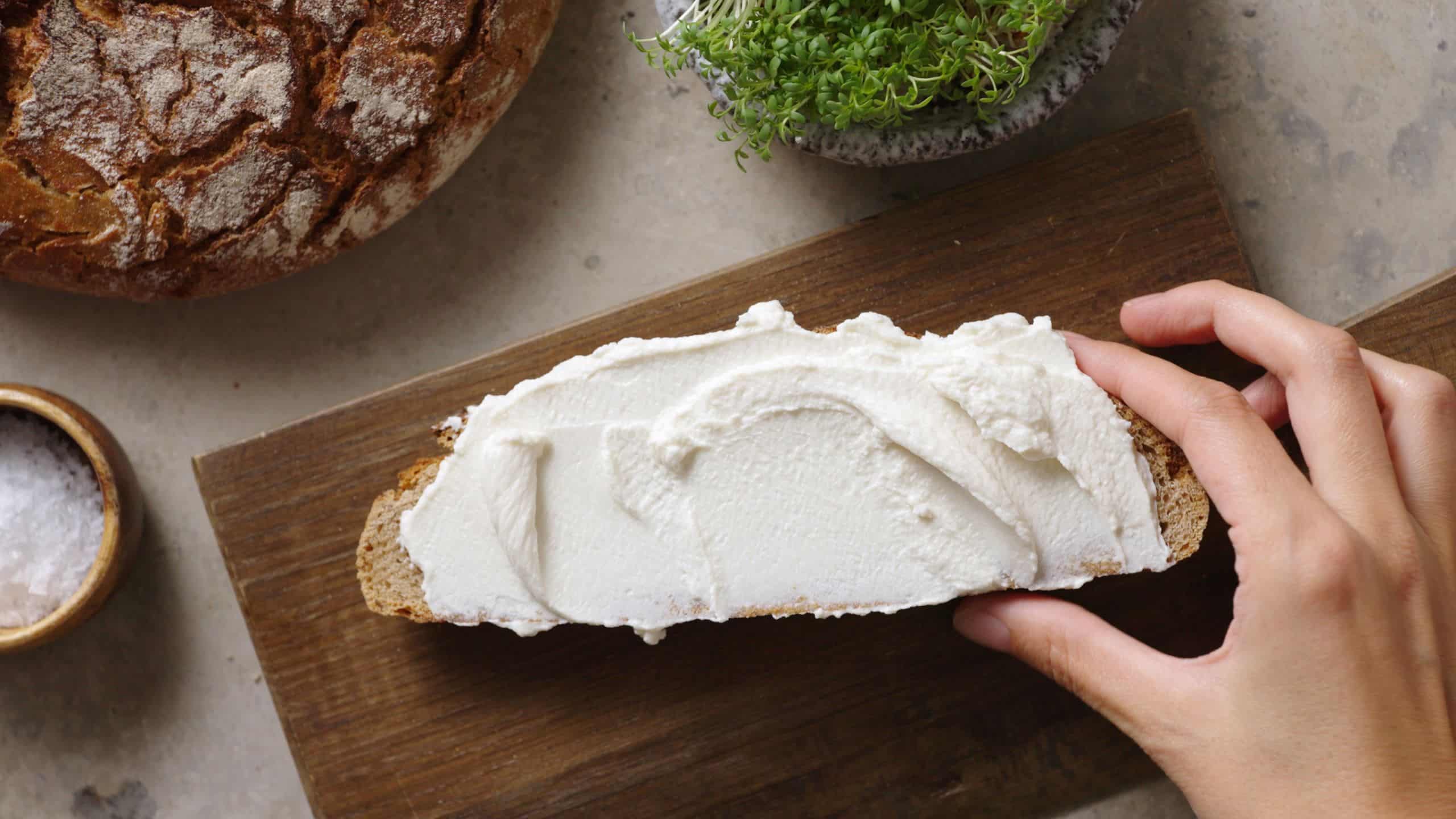 Hand mit Scheibe Brot auf dem die Frischkäsealternative Formo Bio verstrichen ist.
