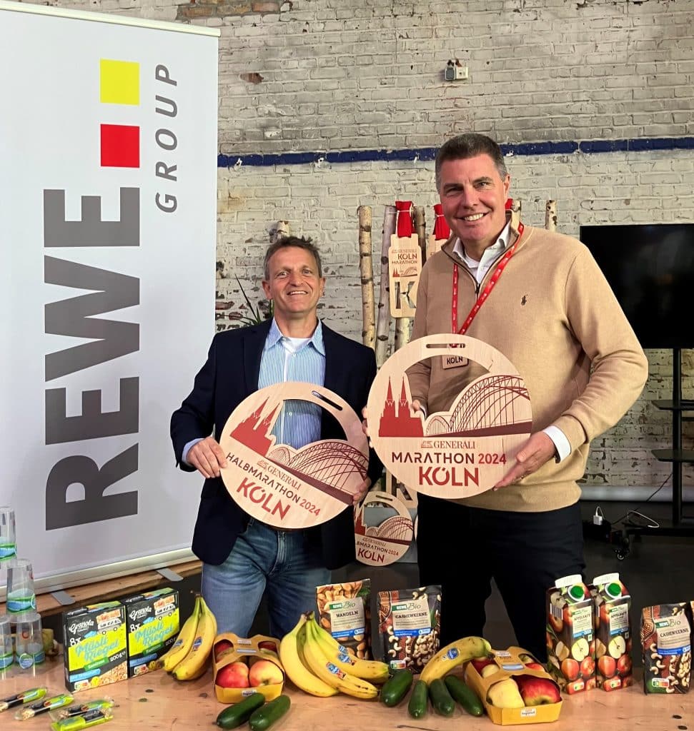 v.l.n.r.: Markus Frisch, Geschäftsführer der Kölner AusdauerSport GmbH, Sven Spork, Bereichsvorstand der REWE Group halten den Preis des Marathons 2024 als Symbol.