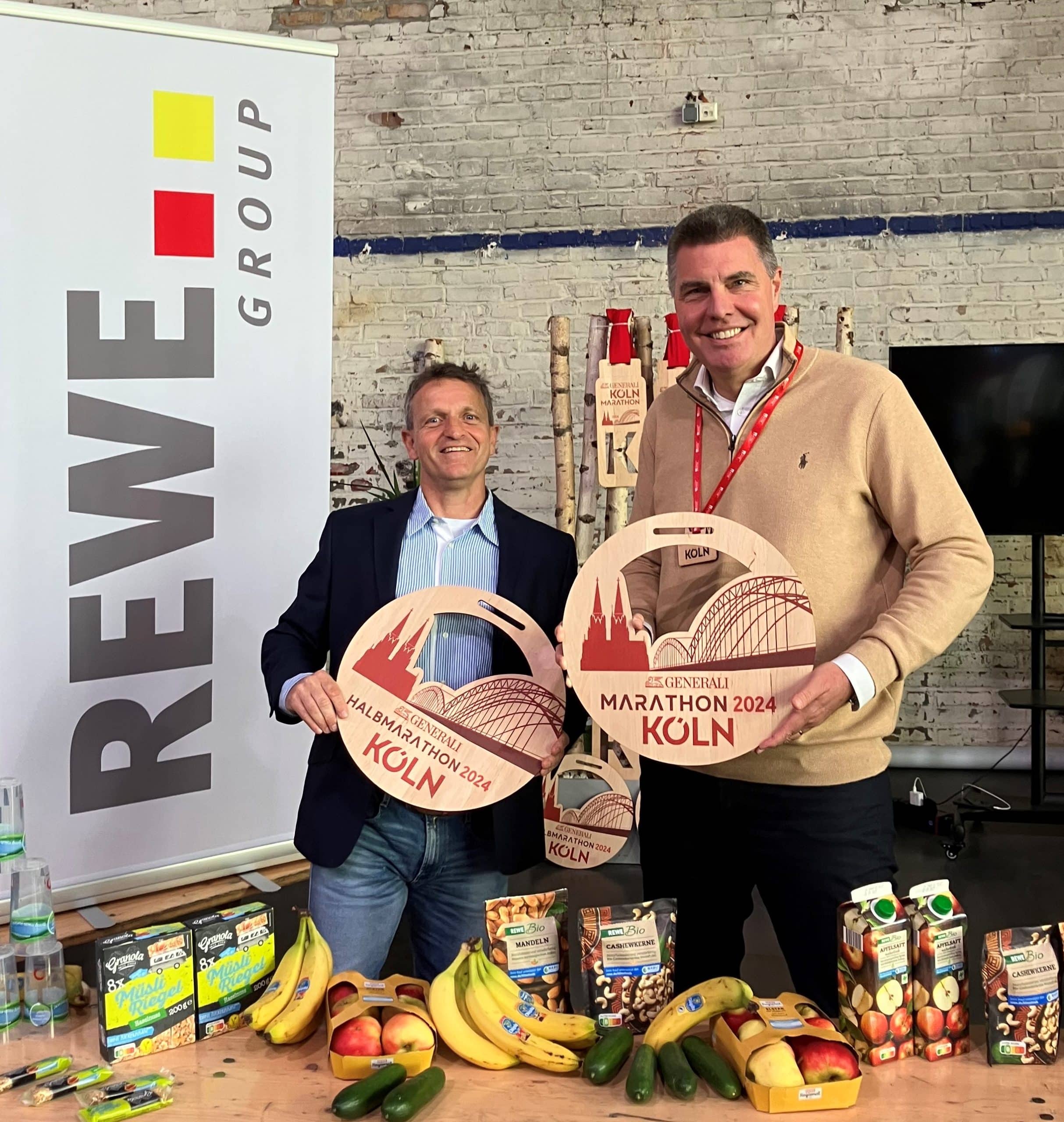 v.l.n.r.: Markus Frisch, Geschäftsführer der Kölner AusdauerSport GmbH, Sven Spork, Bereichsvorstand der REWE GROUP halten den Preis des Marathons 2024 als Symbol.