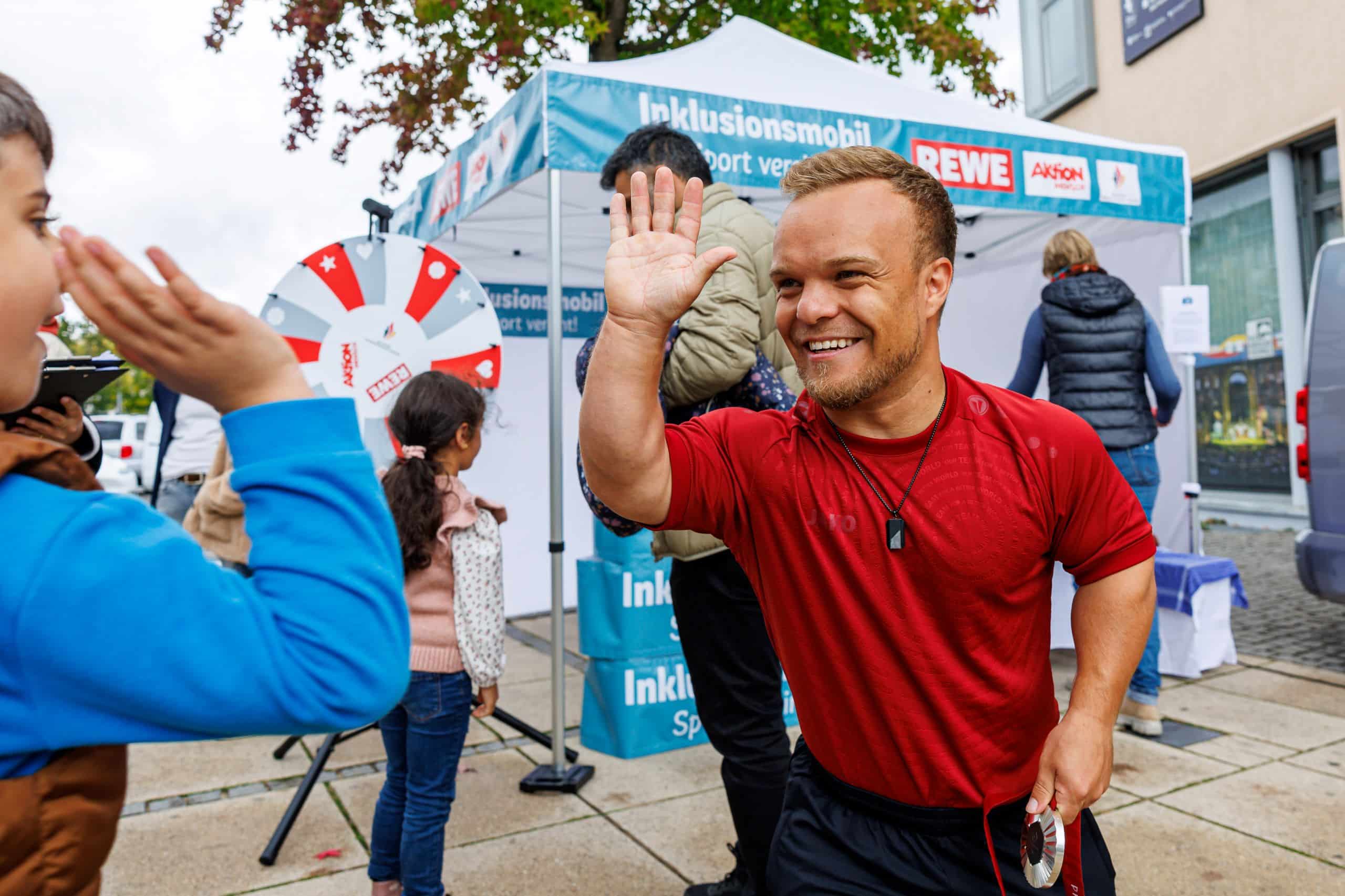 Niko Kappel als Botschafter des Inklusionsmobils der einem Kind High Five gibt.