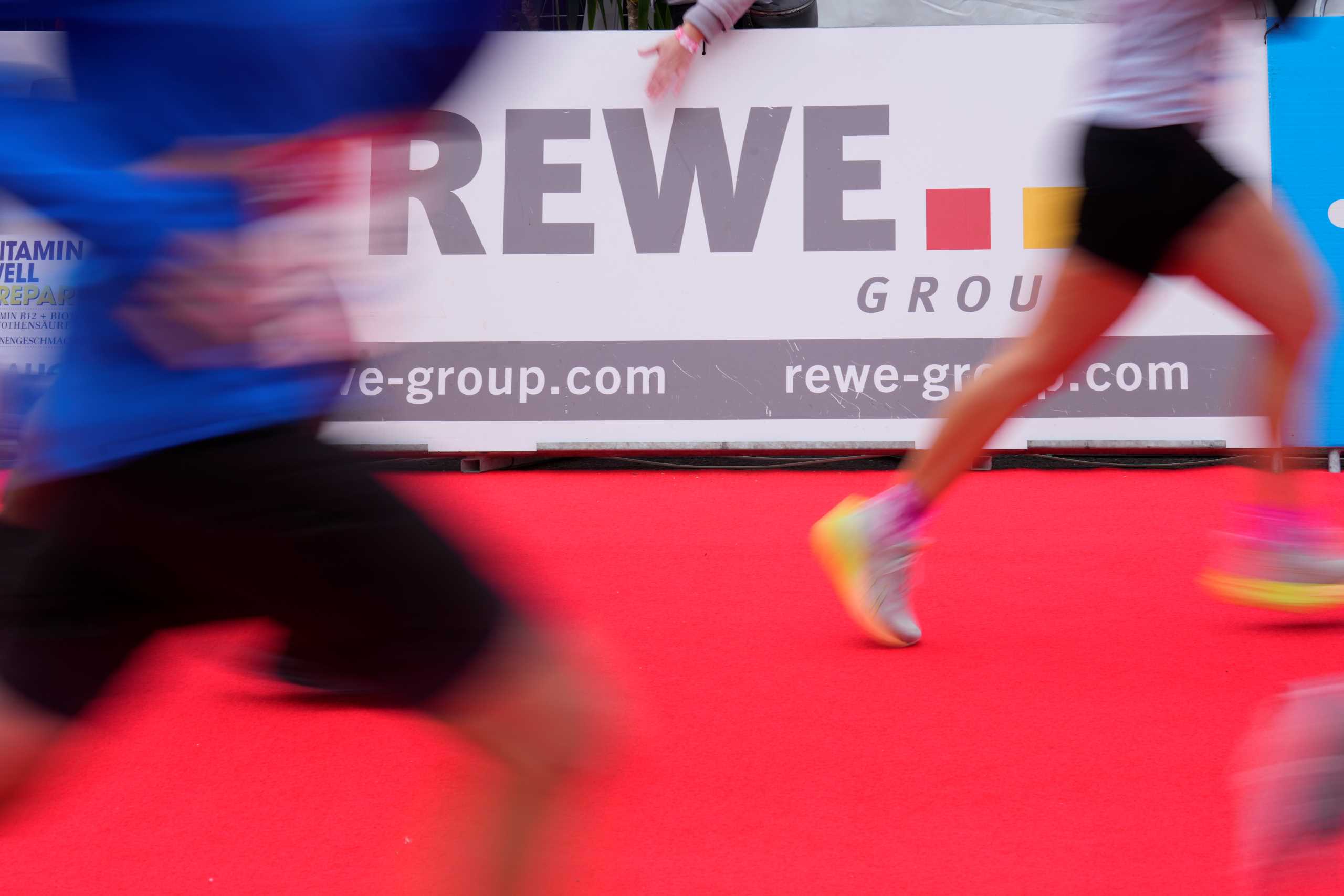 REWE Group Logo mit laufenden Menschen davor