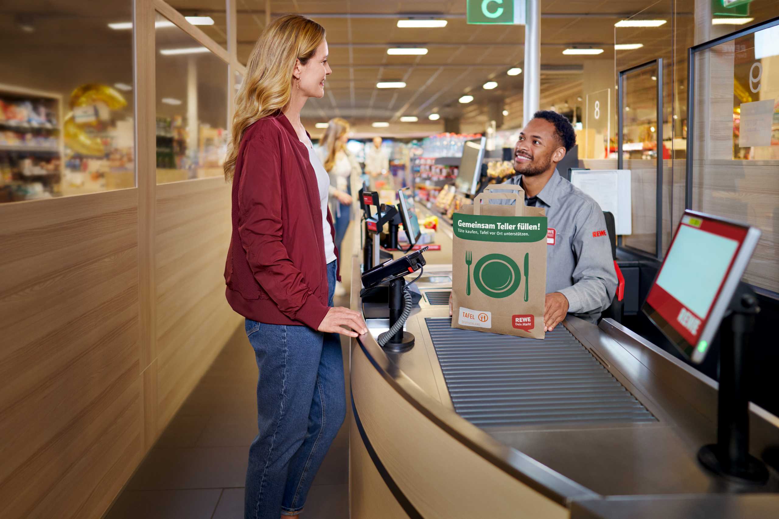 Frau steht an der Kasse mit einem Kassierer eines Supermarktes und kauft eine Tafeltüte.