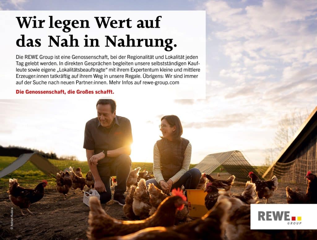 Eine Frau und ein Mann füttern Hühner auf einer Wiese eines Bauernhofes.