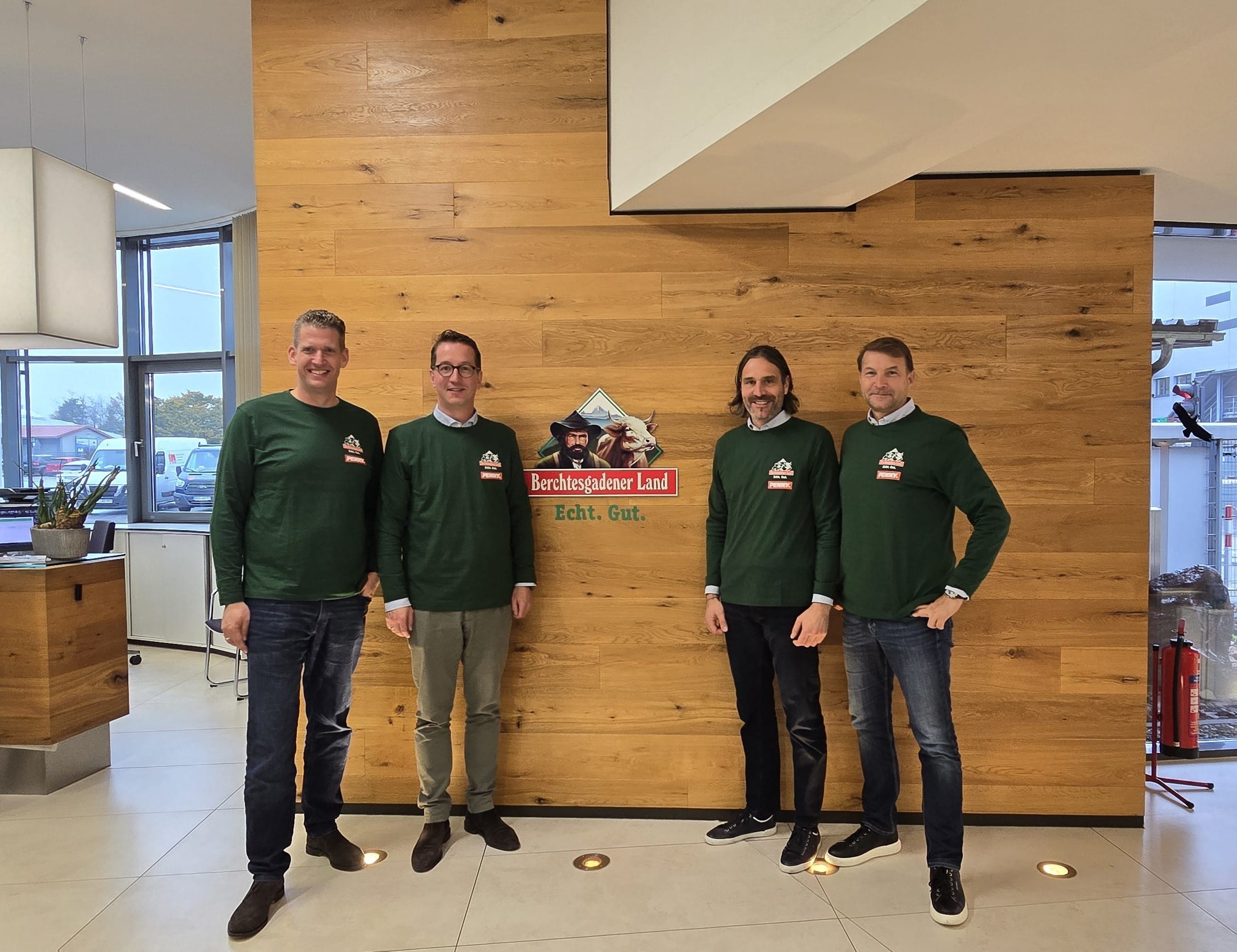 Stefan Görgens, Philipp Stiehler, Bernhard Pointner und Hans-Jürgen Moog stehen vor einer Wand mit dem Logo der Molkerei Berchtesgadener Land.
