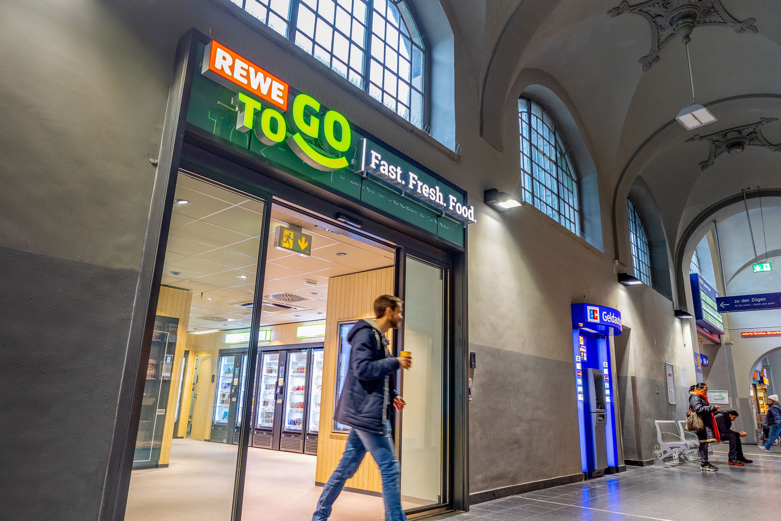 Mensch der einen REWE To Go Laden verlässt