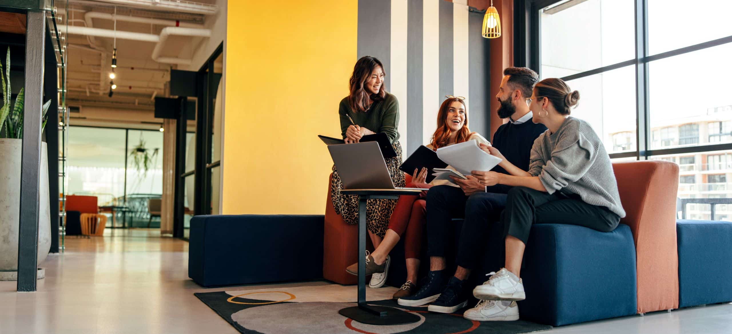 Ein Mann und drei Frauen sitzen zusammen im Büro und unterhalten sich lachend.