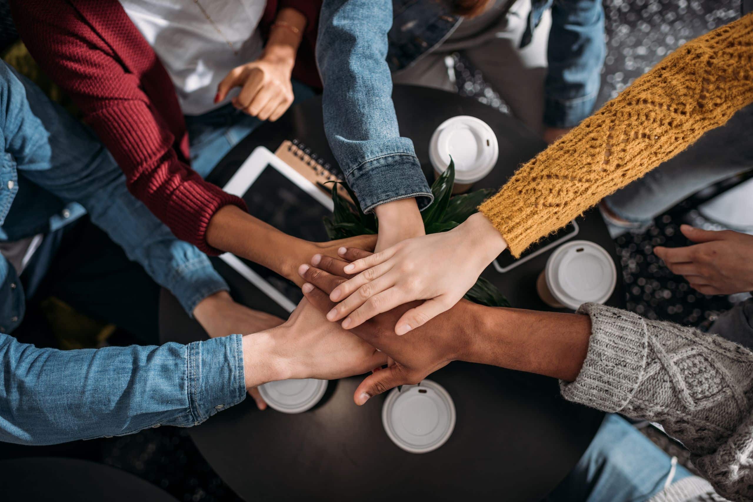 5 Menschen halten ihre Hände zusammen in ihre Mitte, um Zusammenhalt zu zeigen.