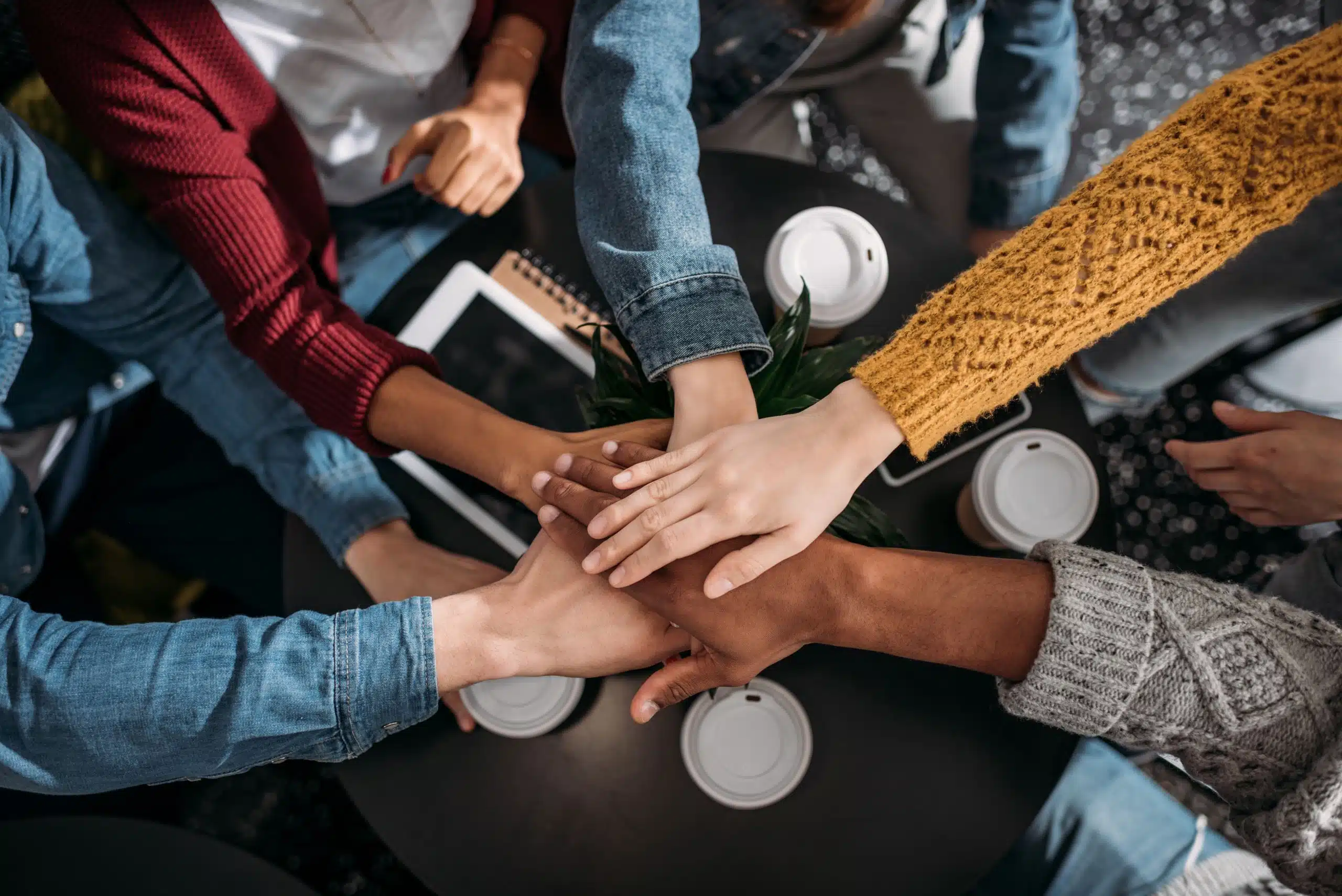 5 Menschen halten ihre Hände zusammen in ihre Mitte, um Zusammenhalt zu zeigen.