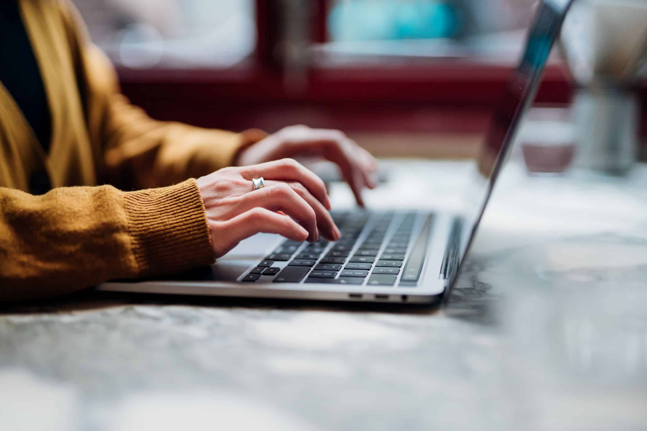 Nahaufnahme einer Person die auf einem aufgeklappten Laptop auf der Tastatur tippt.