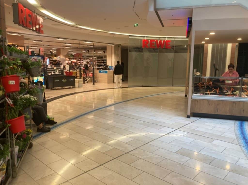 Außenansicht eines REWE Marktes in einem Einkaufszentrum.