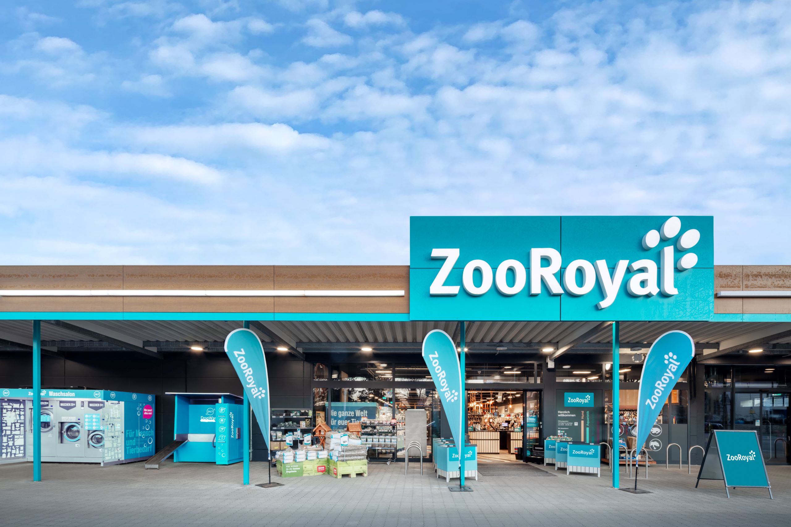 Exterior view of a ZooRoyal store with dog washing station and launderette in front of the entrance.