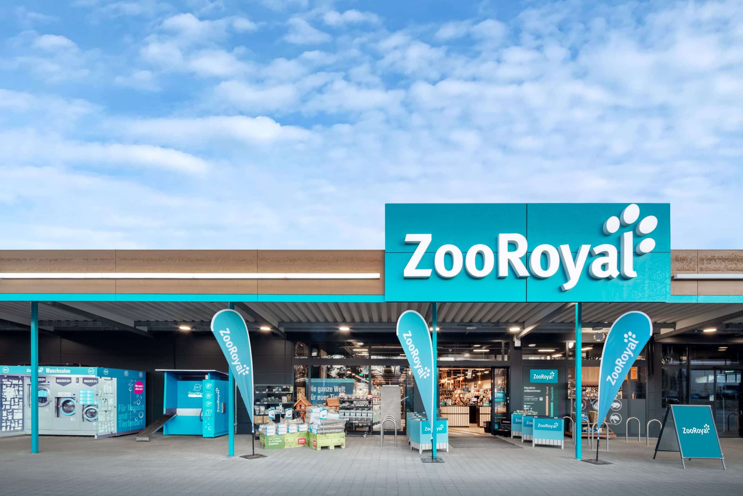 Exterior view of a ZooRoyal store with dog washing station and launderette in front of the entrance.
