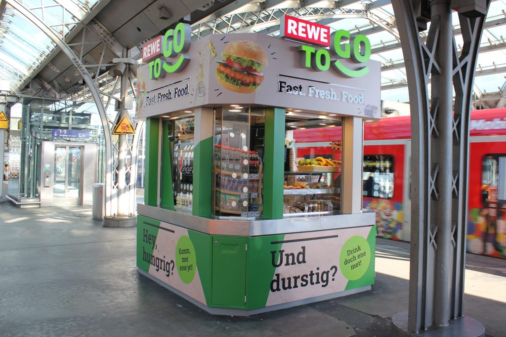 Exterior view of the REWE To Go platform kiosk at Cologne Central Station.