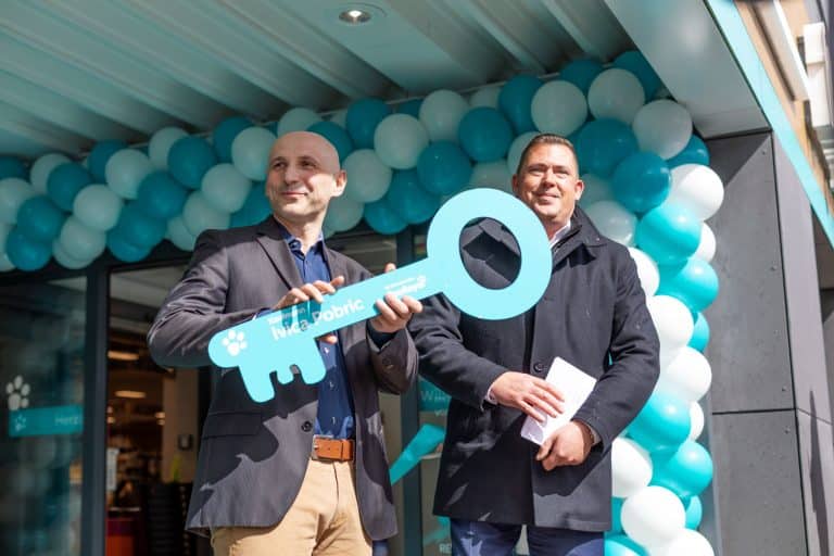 ZooRoyal Kaufmann Ivica Pobric hält einen großen blauen Schlüssel aus Pappe in den Händen, anlässlich der Eröffnung seines ZooRoyal Marktes, der mit Luftballons geschmückt im Hintergrund zu sehen ist. Neben ihm steht Jochen Vogel, Vorsitzender der Geschäftsleitung Region Nord.