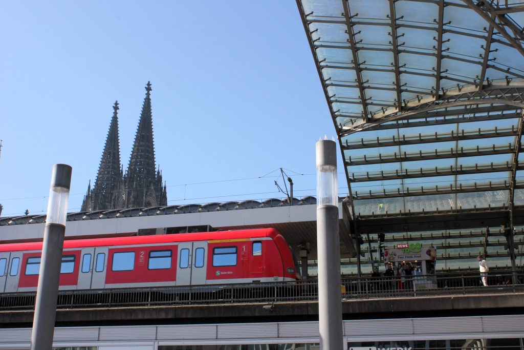 Picture from below looking up at the REWE To Go rail kiosk at Cologne Central Station with Cologne Cathedral in the background.